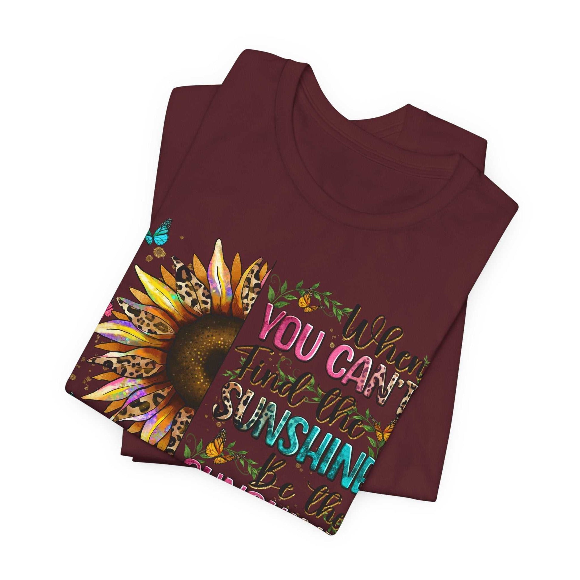 Folded maroon Sunshine Quote Tee with vibrant sunflower and inspirational text design on front