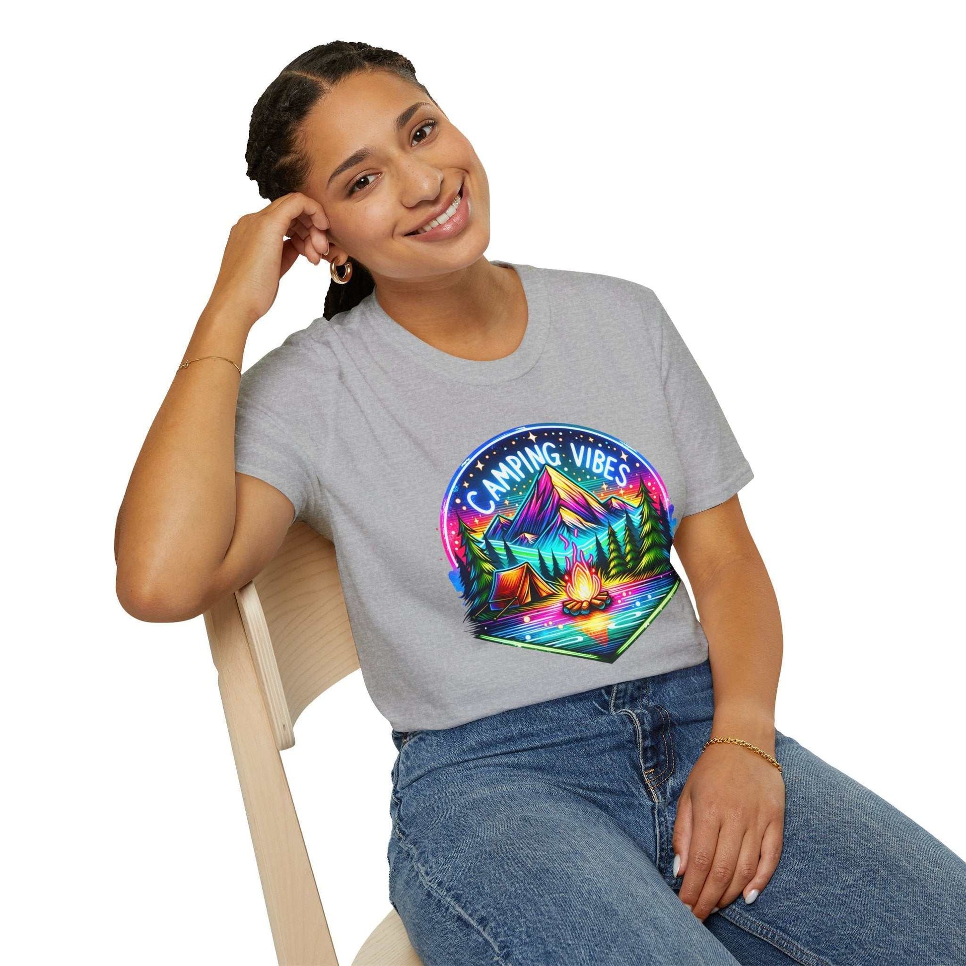 Woman wearing gray Camping Vibes Unisex softstyle t-shirt with colorful camping scene graphic sitting on chair smiling