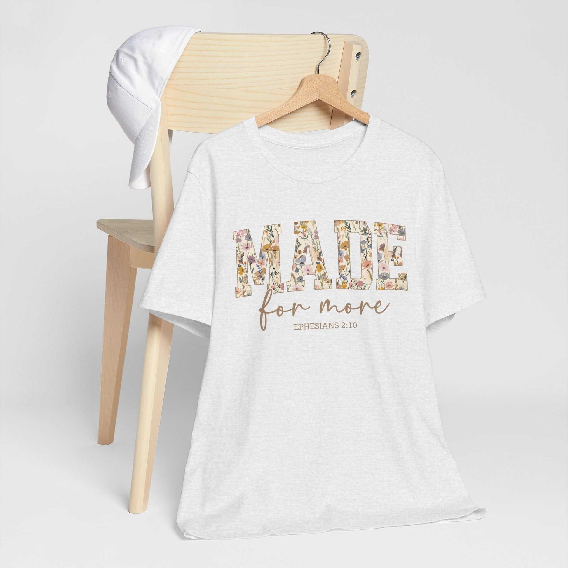 White "Made for More" floral print unisex tee hanging on chair with white cap.