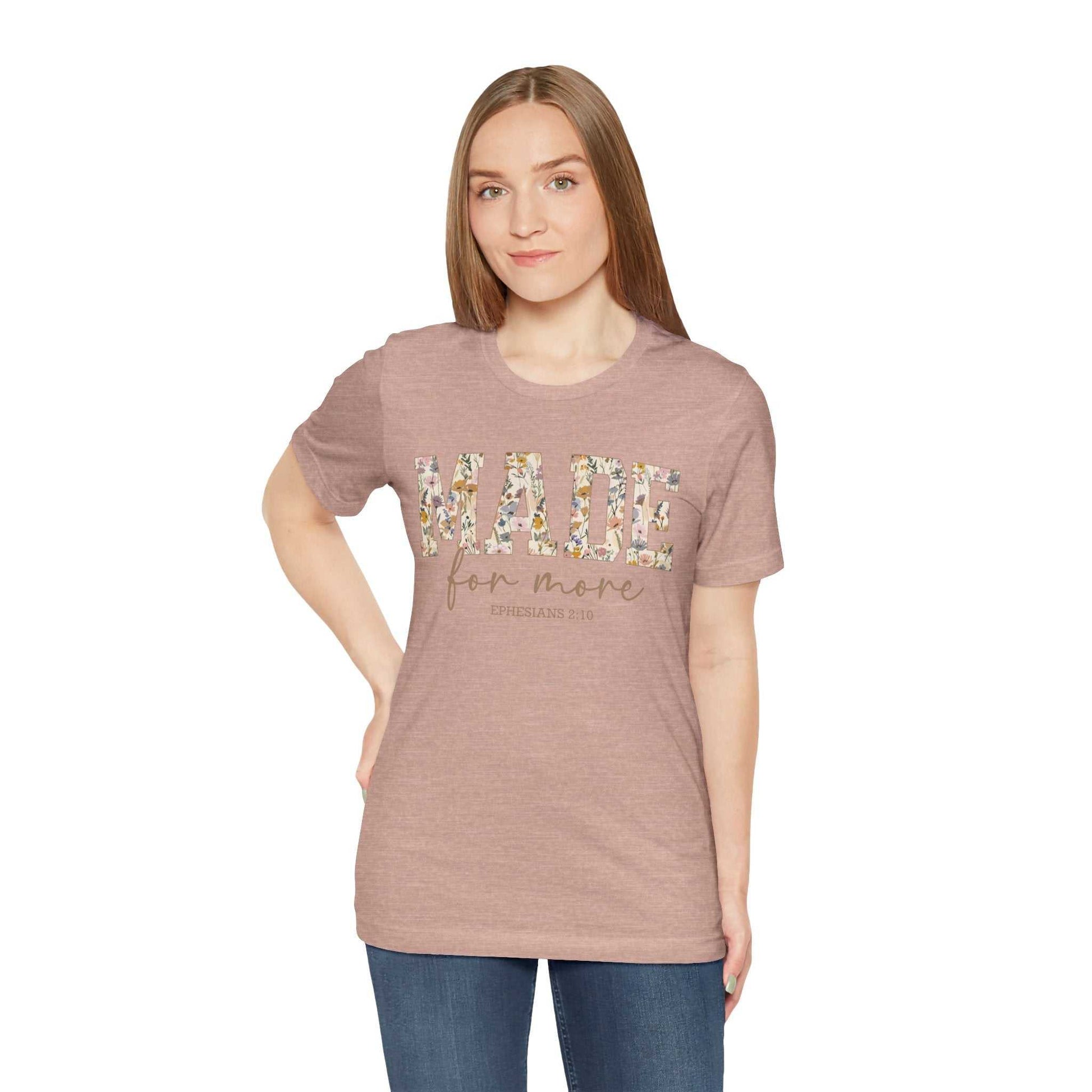 Woman wearing a dusty rose "Made for More" unisex jersey short sleeve tee with floral print lettering, styled with jeans.