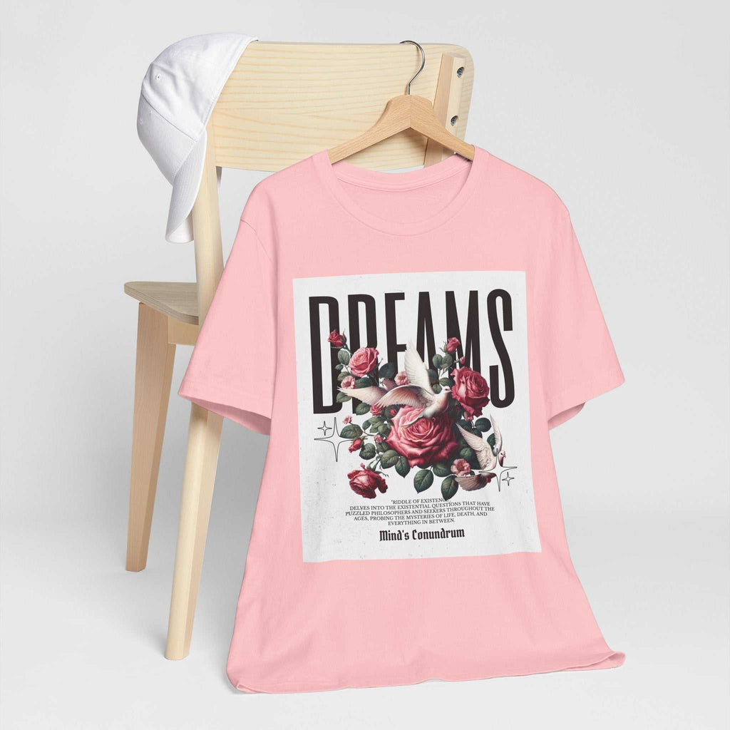 Pink unisex Dreams Floral Tee with rose graphic and bold typography hanging on wooden chair with white cap
