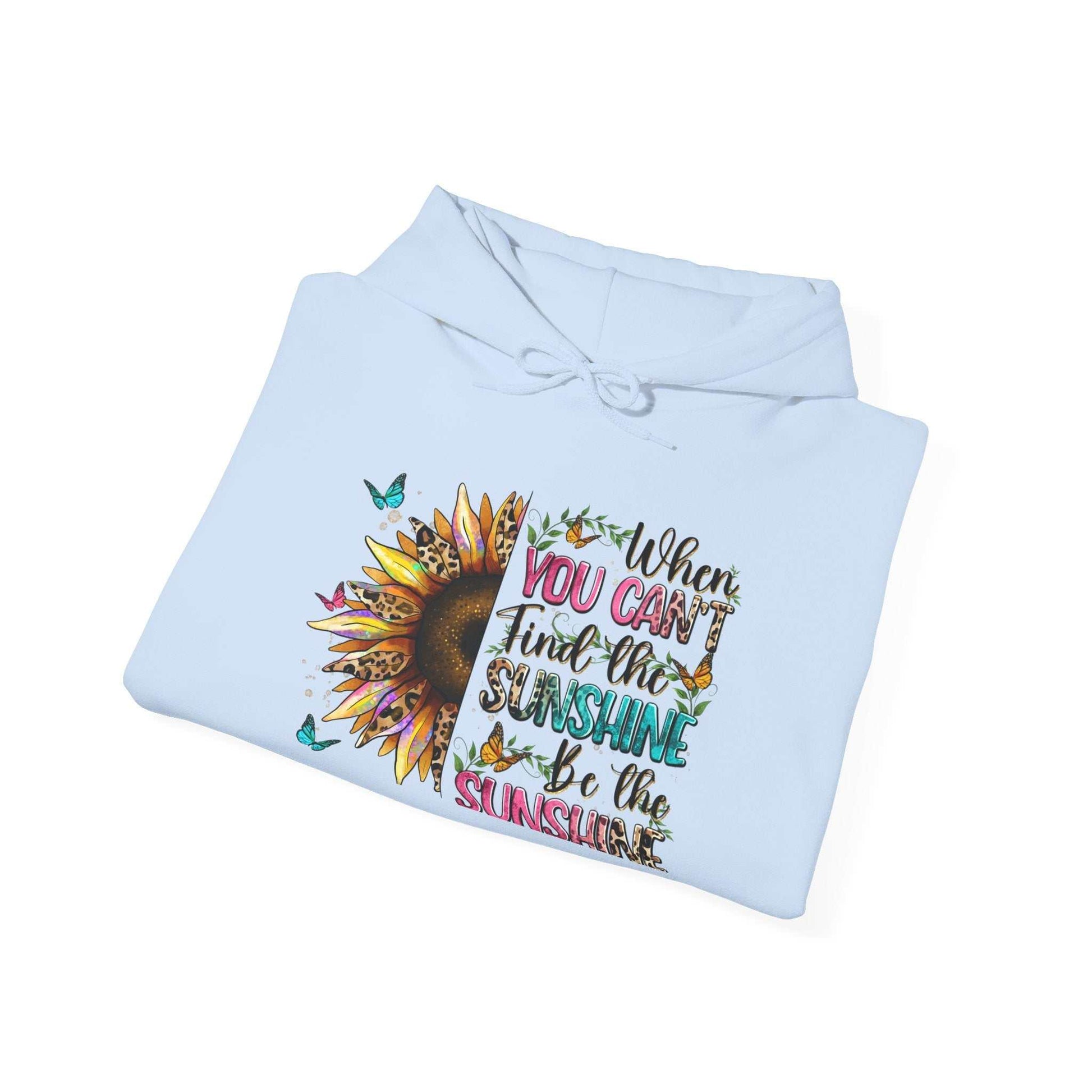 Folded light blue hoodie with sunflower graphic and inspirational quote "When you can't find the sunshine be the sunshine"