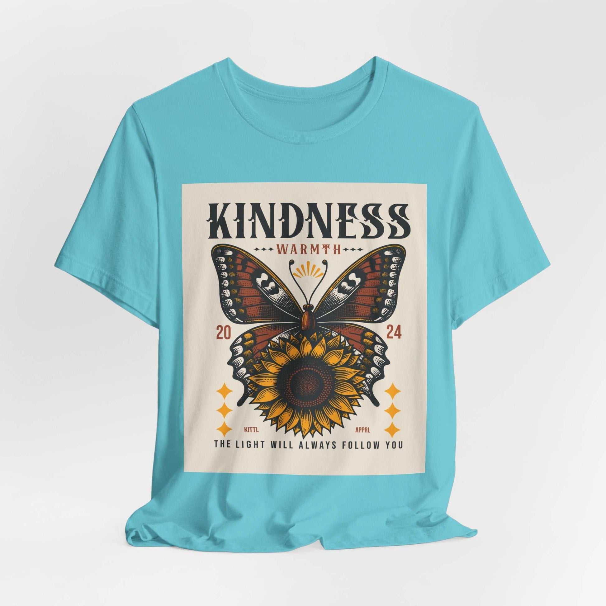 Light blue Kindness Butterfly Tee featuring a butterfly and sunflower design with the words "Kindness Warmth 2024" and the phrase "The light will always follow you" on the front.