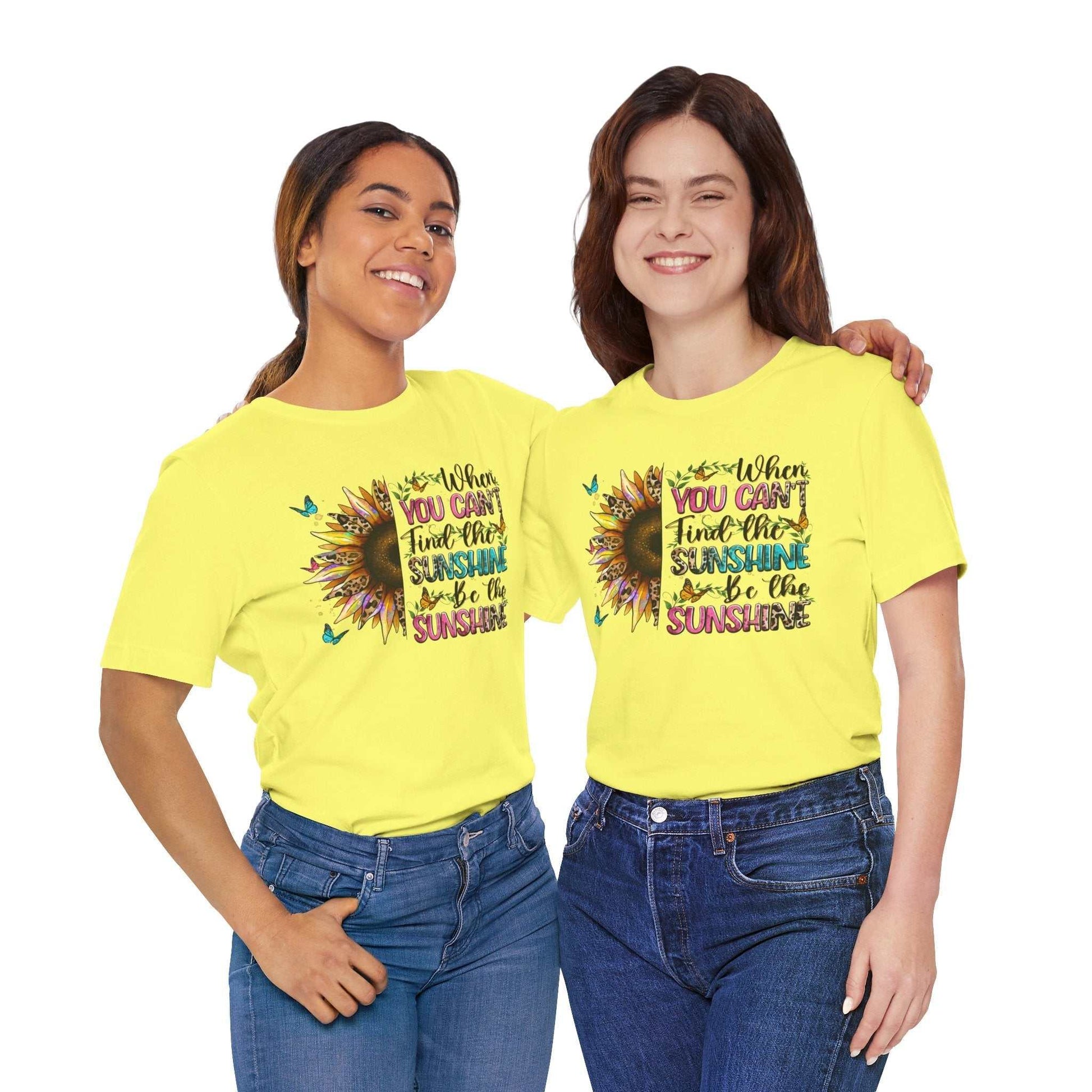 Two women wearing bright yellow Sunshine Quote Tee shirts featuring a colorful sunflower graphic and positive text design.