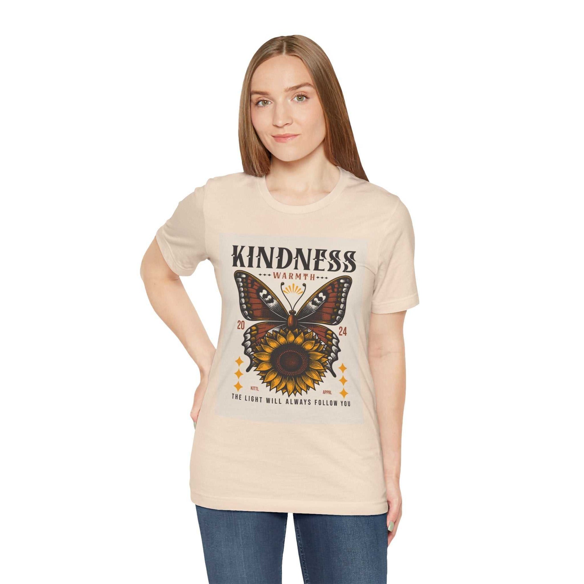 Woman wearing a beige Kindness Butterfly Tee featuring a butterfly and sunflower design with the text "Kindness Warmth 2024 The light will always follow you"