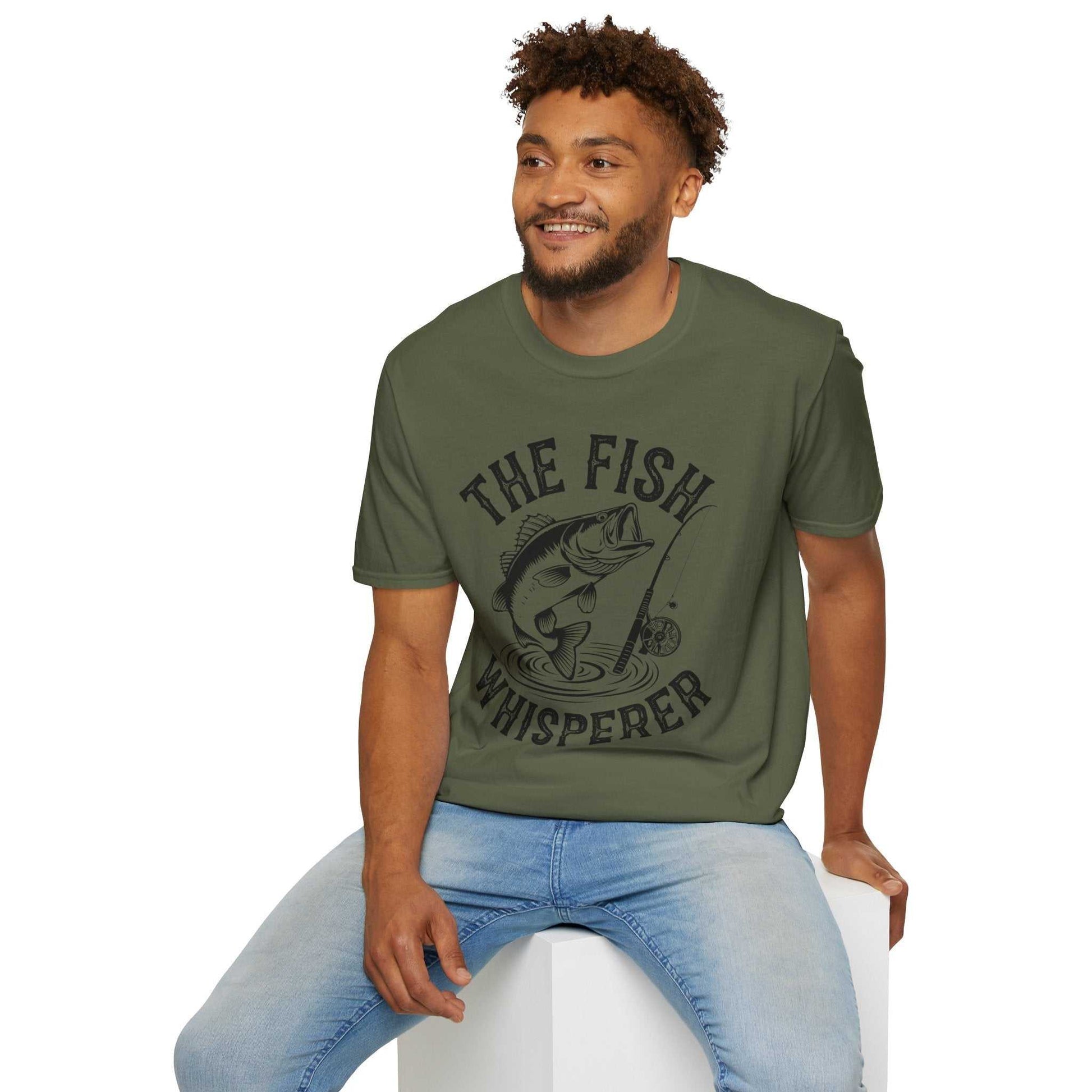 Man wearing olive green unisex softstyle t-shirt with "The Fish Whisperer" fishing graphic and text.