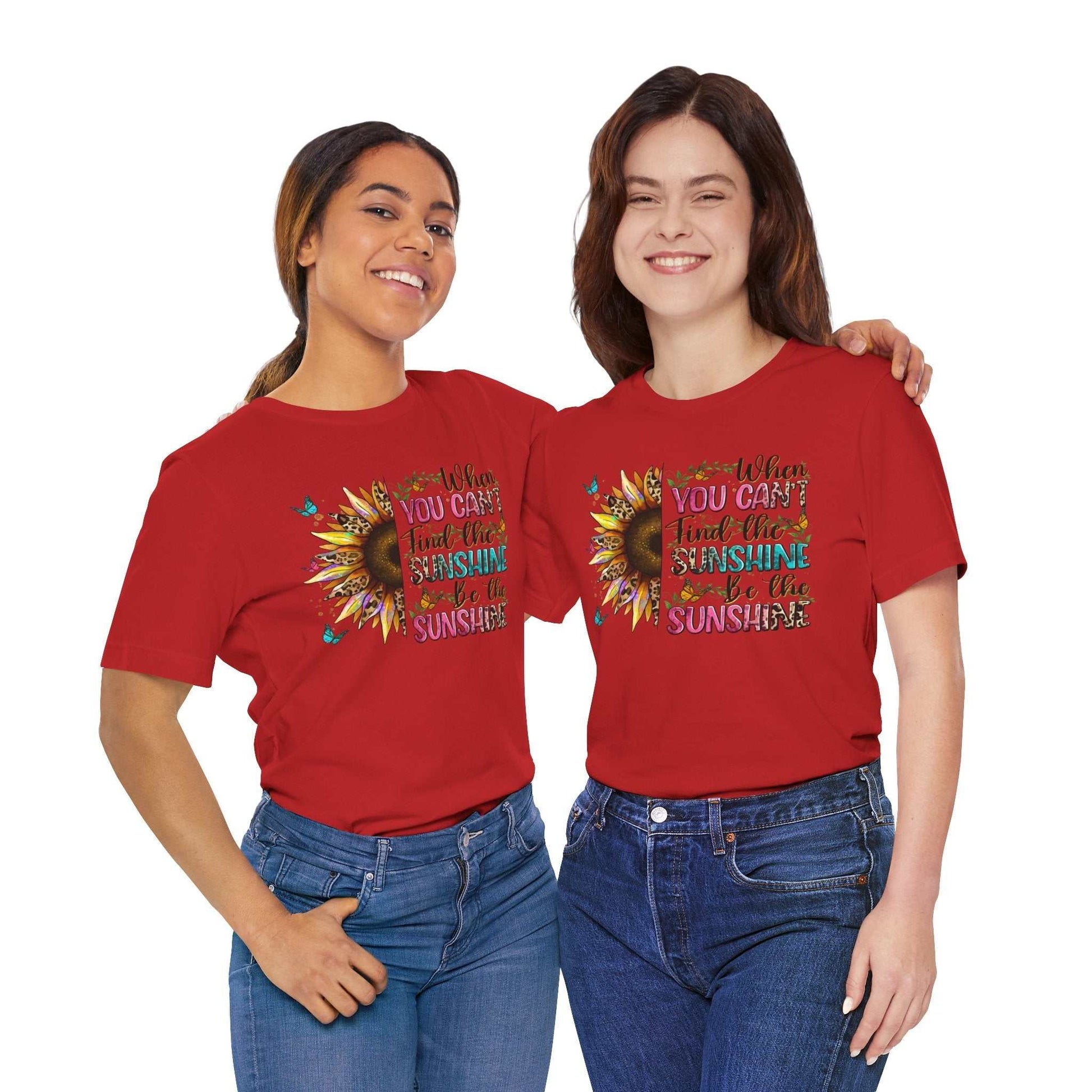 Two women wearing red Sunshine Quote Tee with sunflower and positive message design, styled casually with blue jeans.