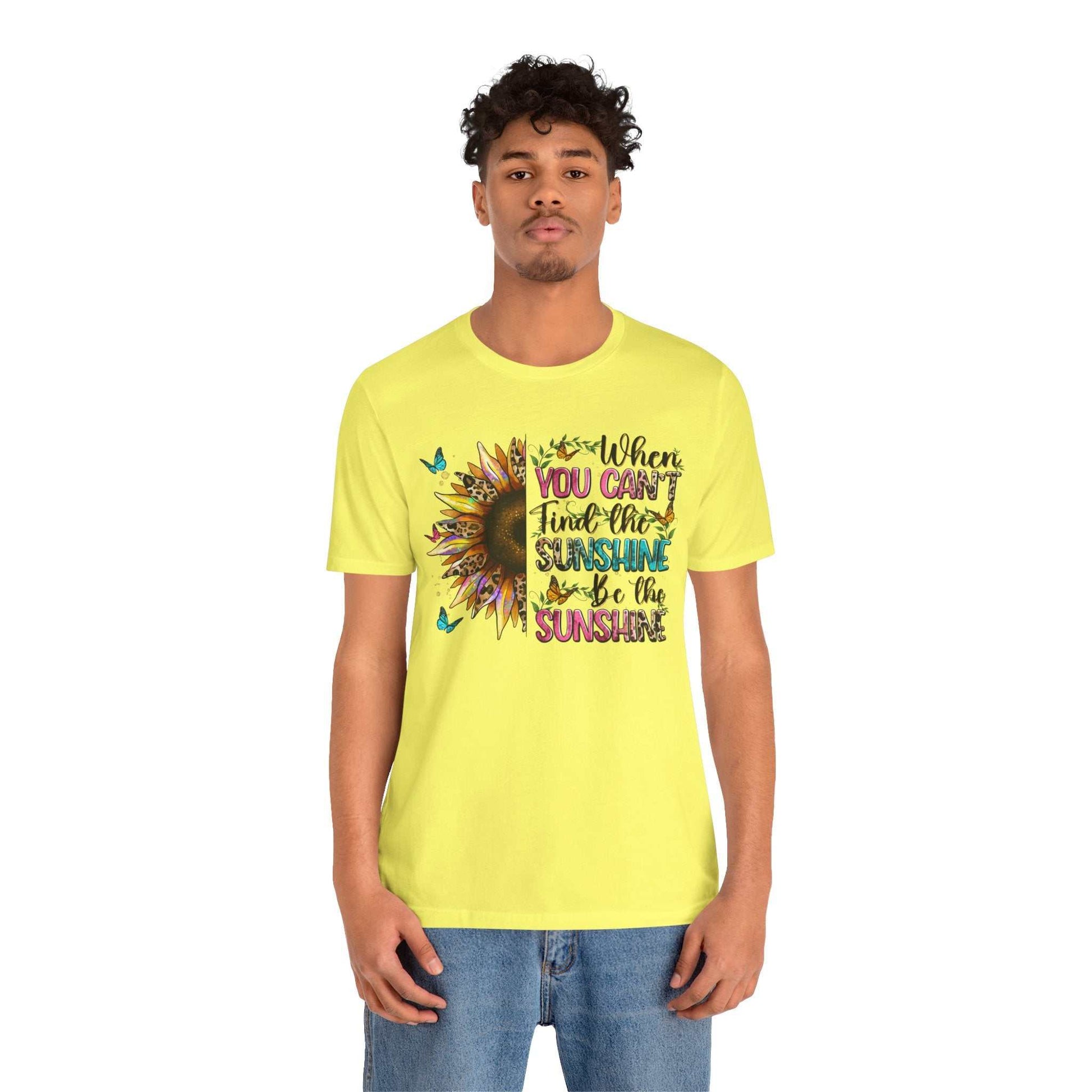 Young man wearing yellow Sunshine Quote Tee with a colorful sunflower and motivational text design on front