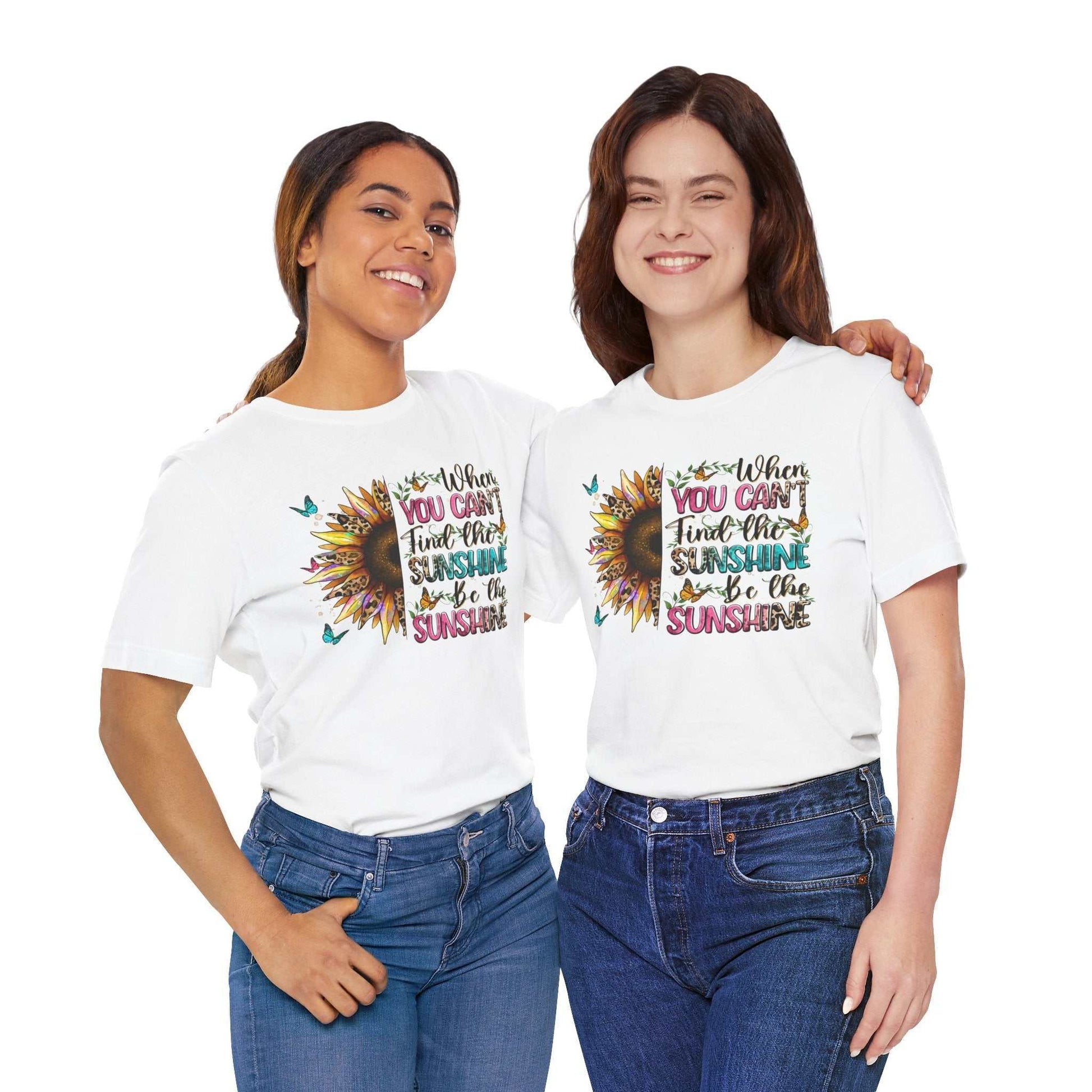 Two smiling women wearing white Sunshine Quote Tee with colorful sunflower and motivational text design, paired with blue jeans