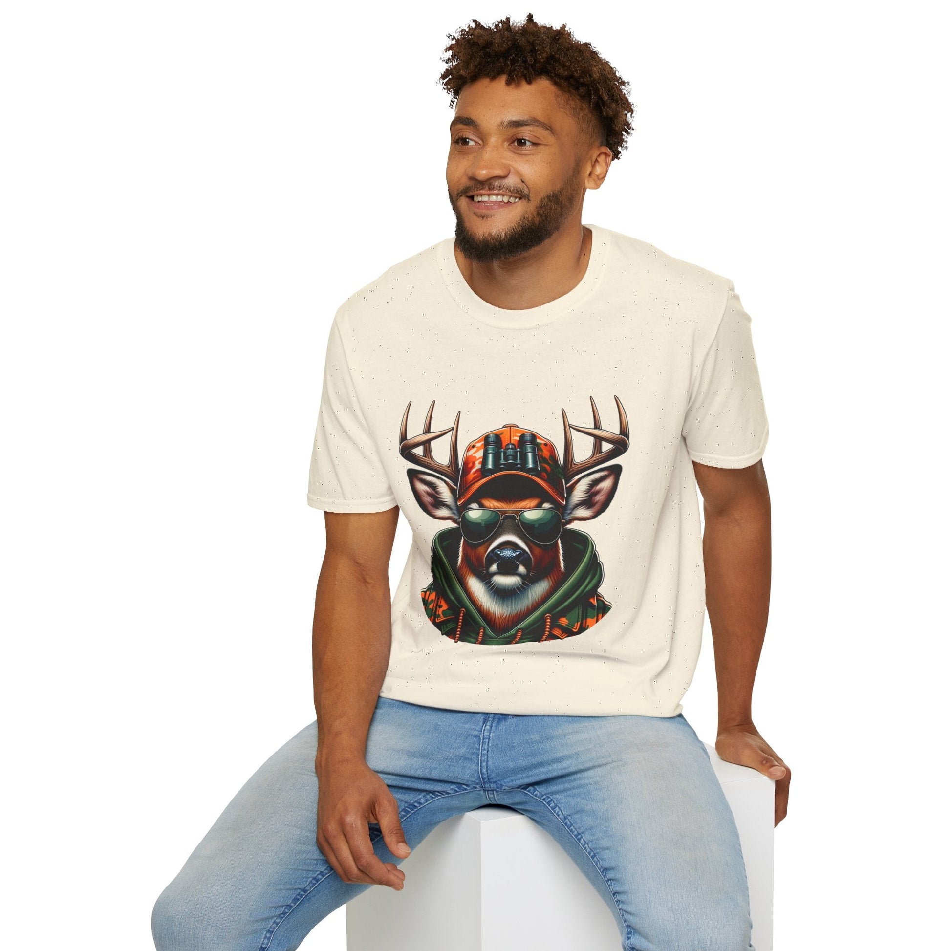 Man wearing a cream unisex softstyle Hunting Enthusiast T-Shirt featuring a deer with sunglasses and camouflage hat graphic.