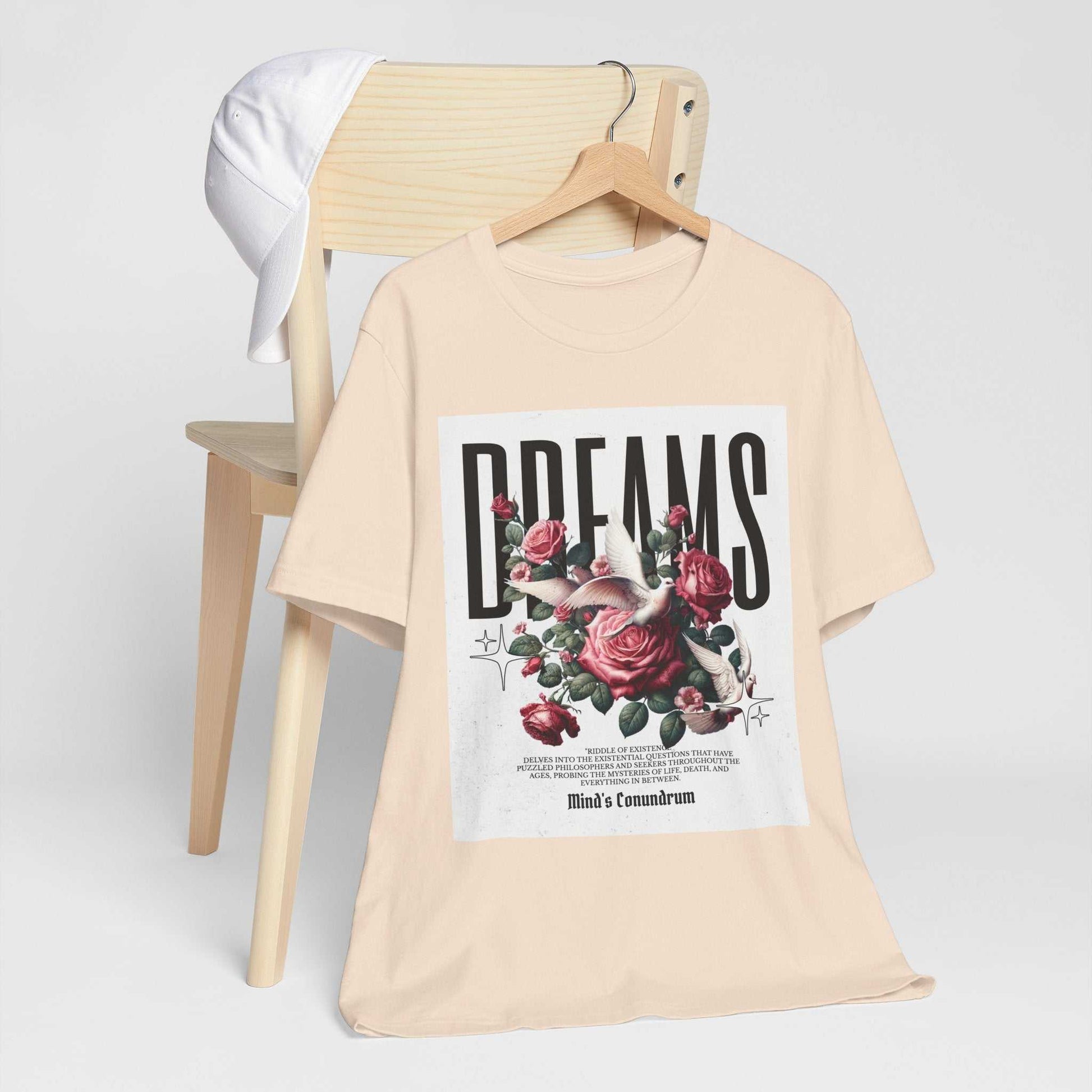 Beige Dreams Floral Tee with vintage rose graphic and bold typography hanging on wooden chair next to white cap