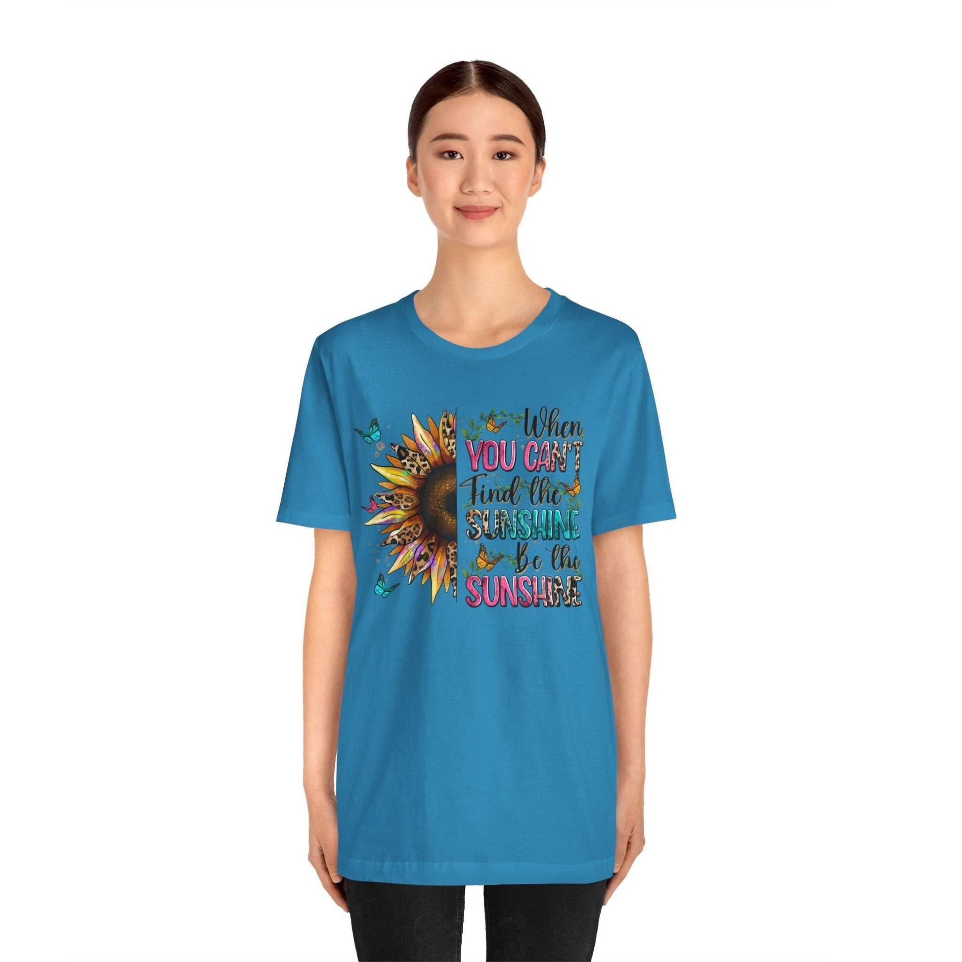 Woman wearing blue Sunshine Quote Tee with sunflower and motivational text design on front