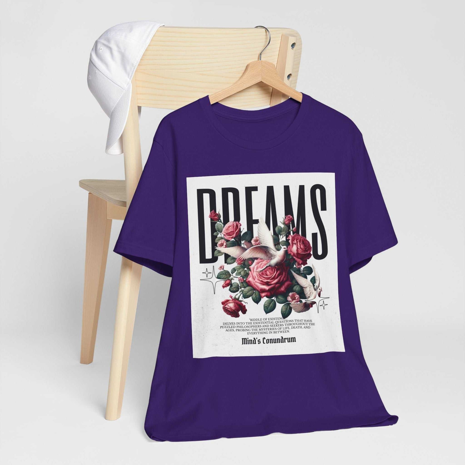 Purple Dreams Floral Tee with bold typography and red rose design, hanging on wooden chair with white cap