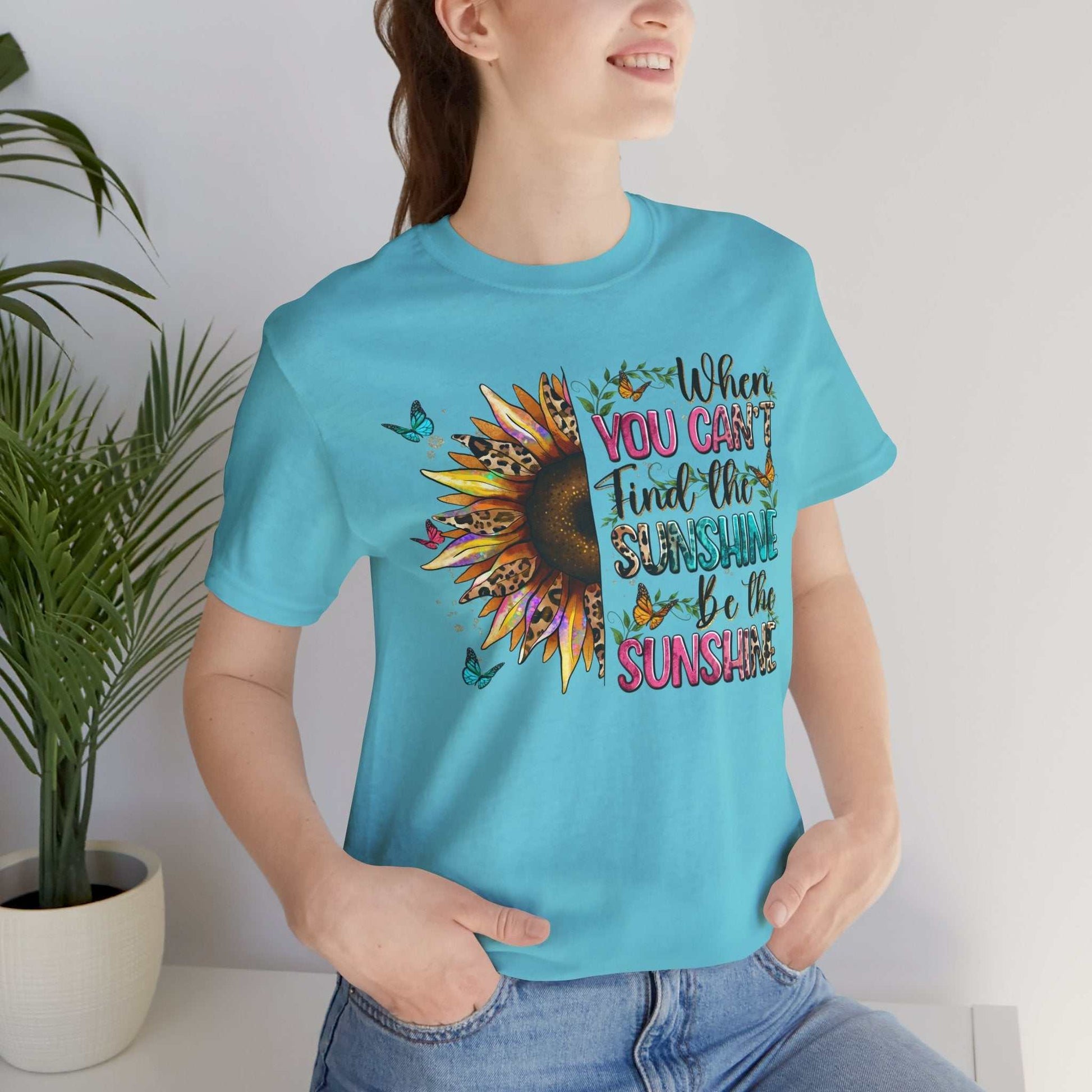 Woman wearing blue Sunshine Quote Tee with sunflower and uplifting message on front