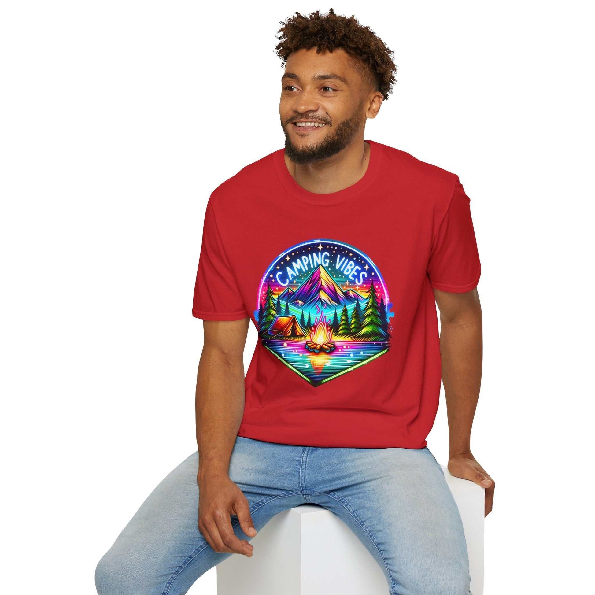 Man wearing red Camping Vibes Unisex softstyle t-shirt with colorful mountain and campfire graphic, sitting casually