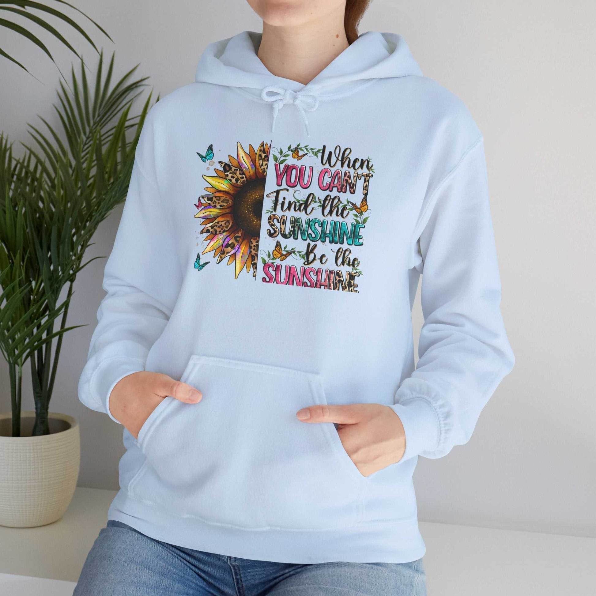Woman wearing light blue sunflower quote hoodie with inspirational sunshine text and butterfly design, front kangaroo pocket and drawstring hood.