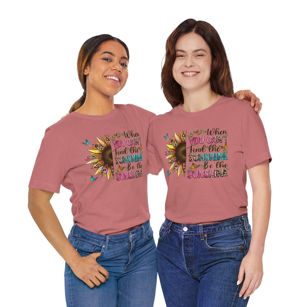 Two women wearing pink Sunshine Quote Tee with sunflower and motivational text design, paired with blue jeans.
