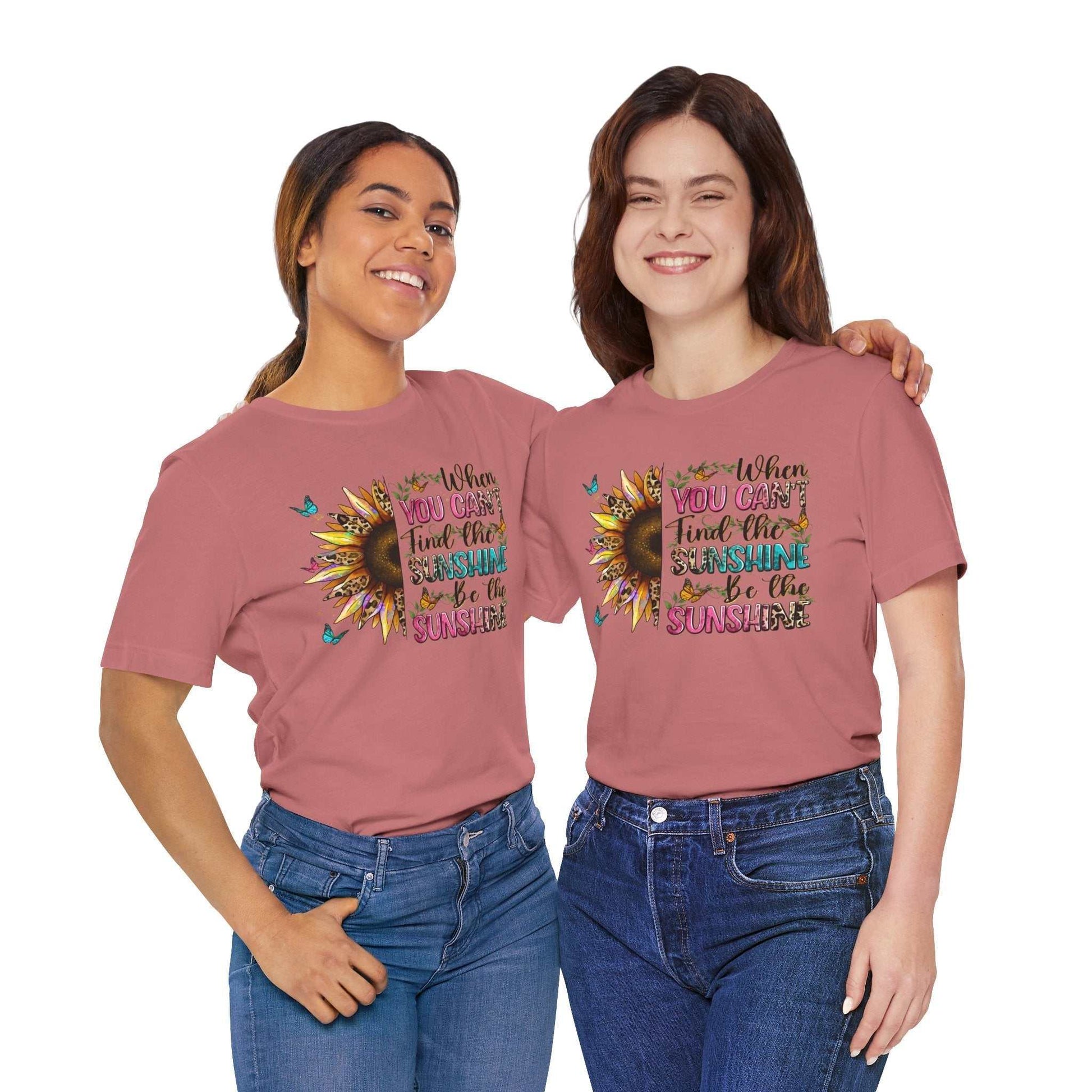 Two women wearing pink Sunshine Quote Tee with sunflower and motivational text design, paired with blue jeans.