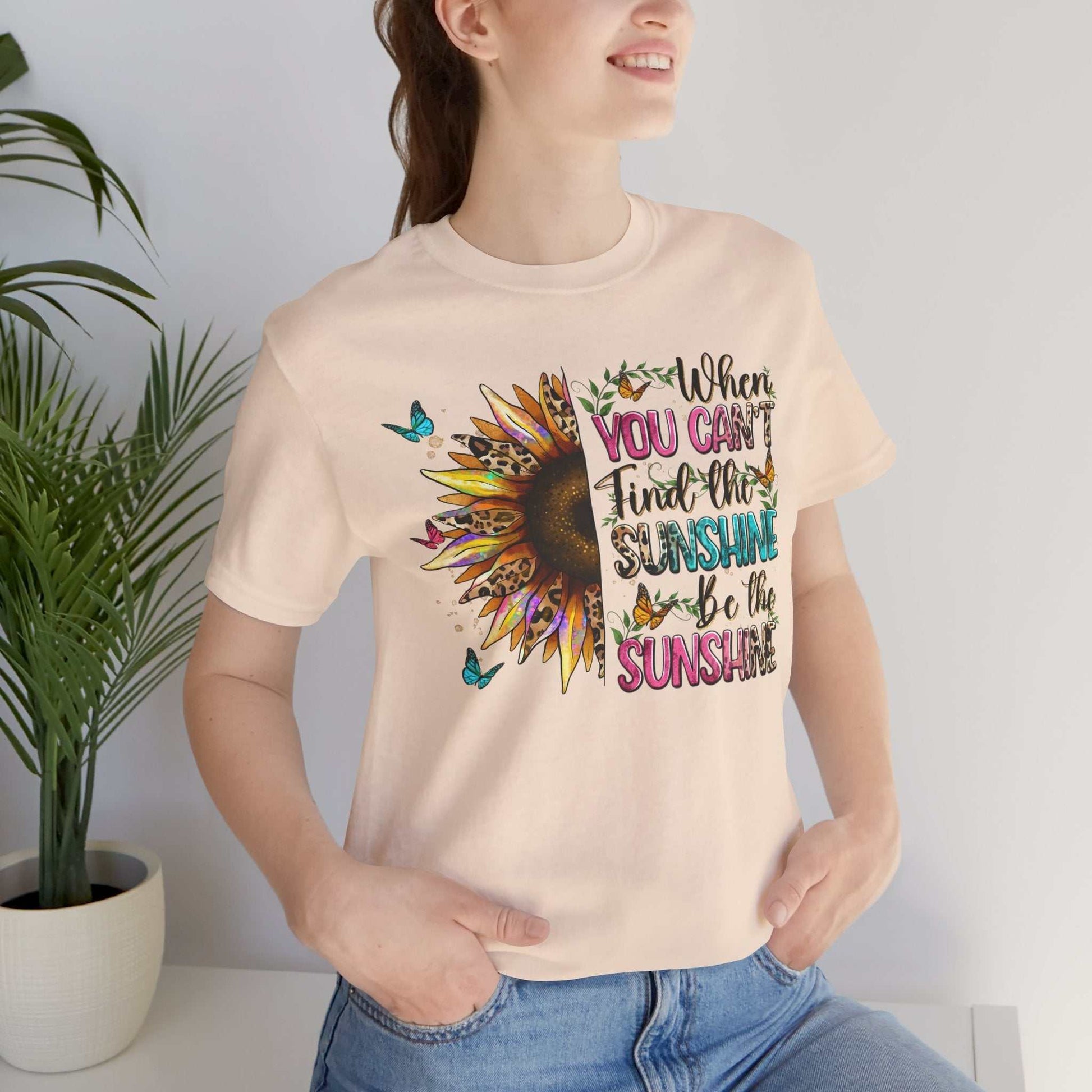 Woman wearing a light-colored Sunshine Quote Tee with a vibrant sunflower and motivational text design.