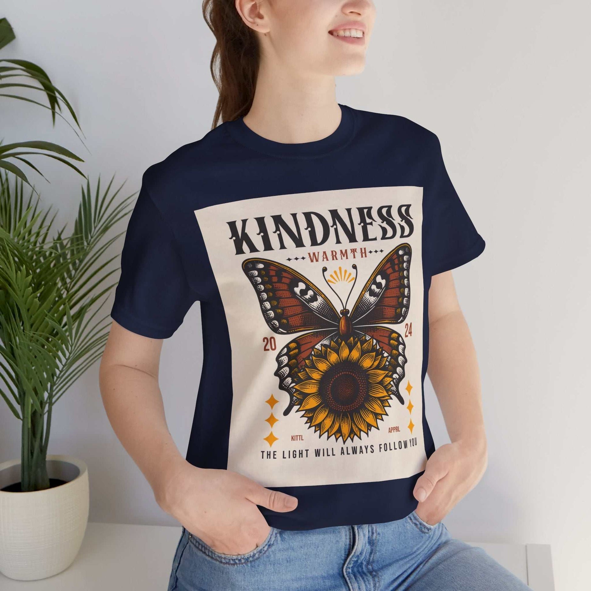 Woman wearing navy Kindness Butterfly Tee with butterfly and sunflower design and text promoting kindness and warmth