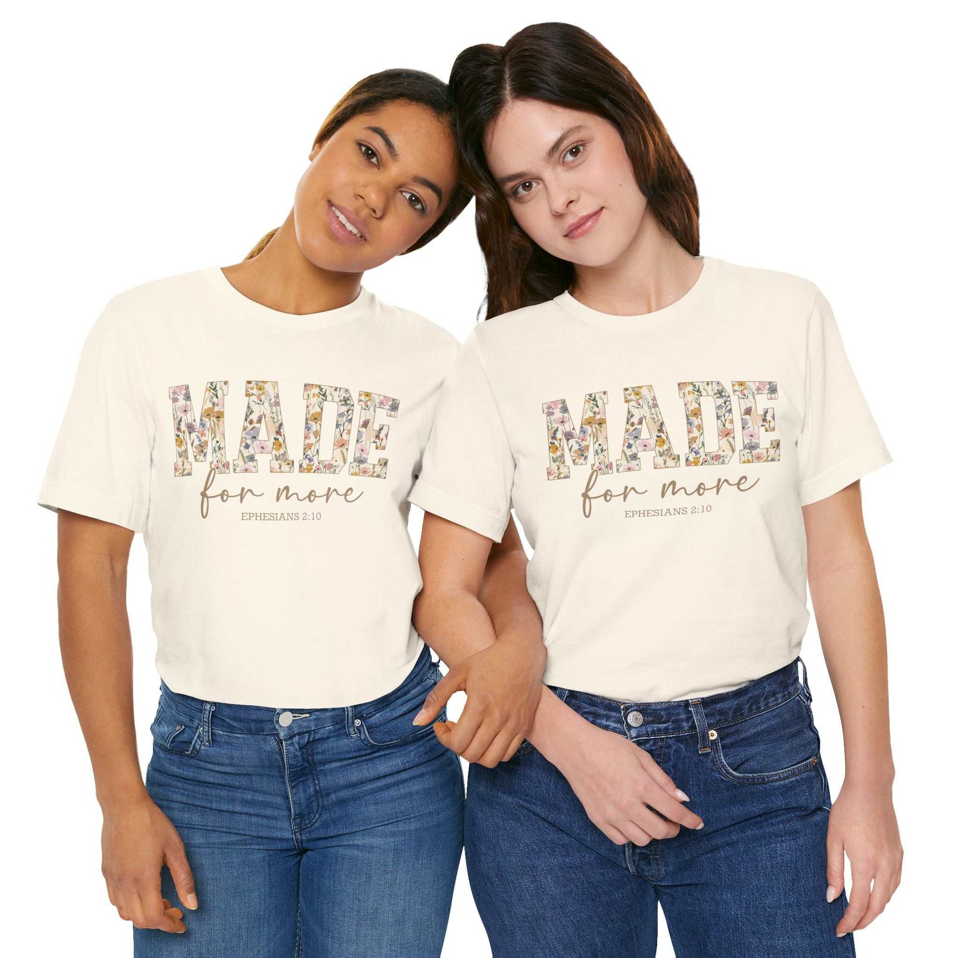 Two women wearing white Made for More Tee shirts with floral text design and scripture reference, styled with jeans.