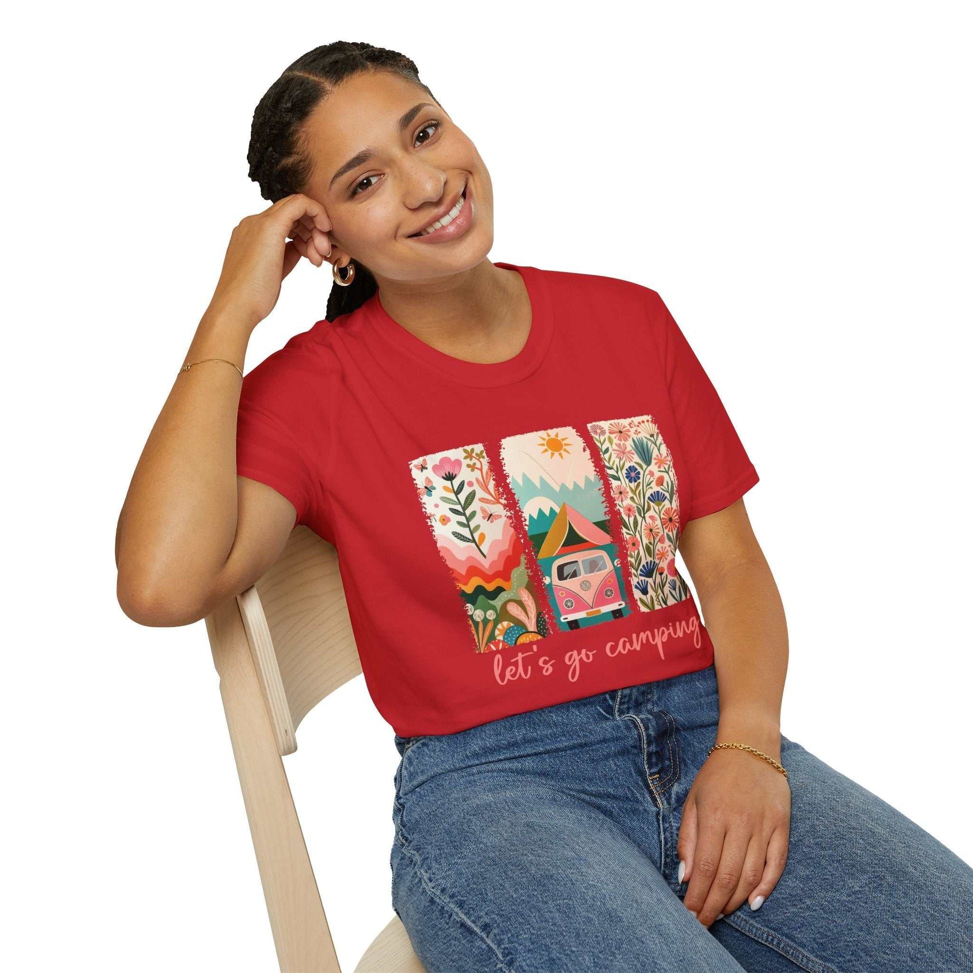 Woman wearing red Camping Adventure unisex softstyle t-shirt with colorful nature and camper van design sitting on chair smiling