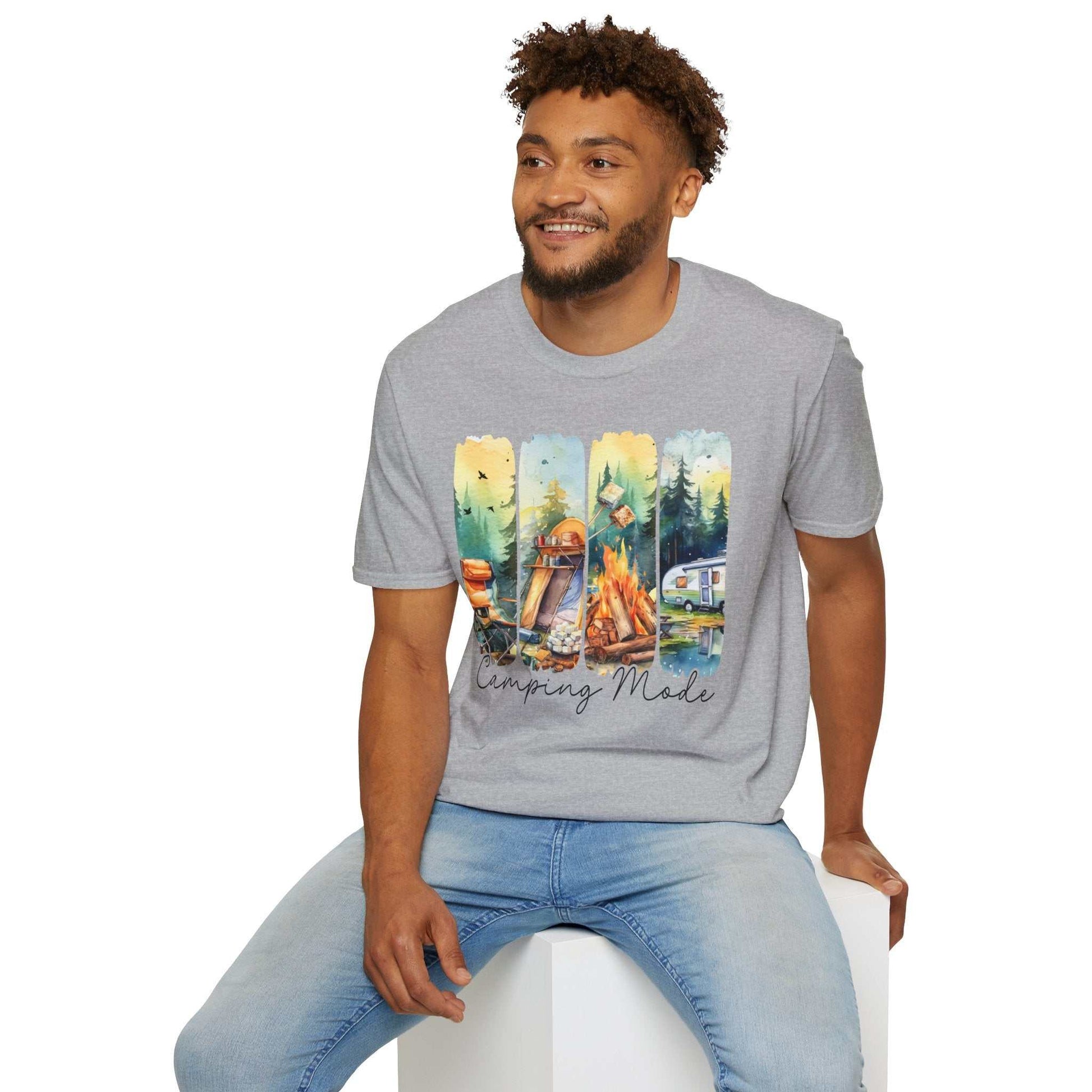Man wearing grey Camping Adventure Unisex T-Shirt with colorful camping-themed graphic and blue jeans sitting on a white block
