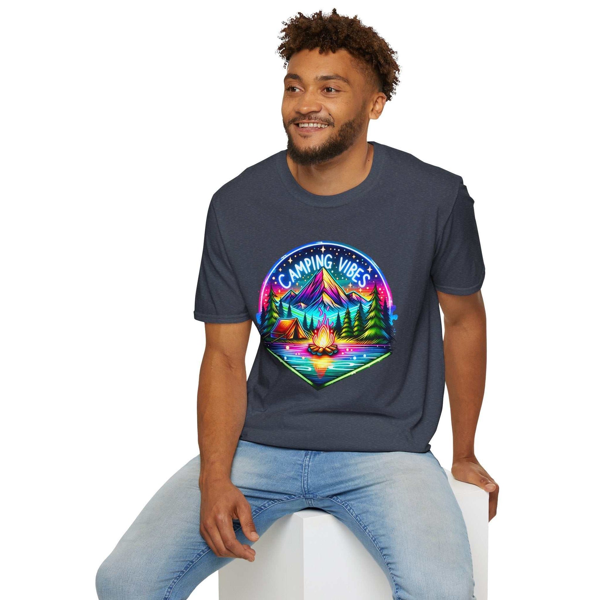 Unisex softstyle t-shirt with colorful camping vibes design featuring mountains, tents, and campfire, worn by smiling man