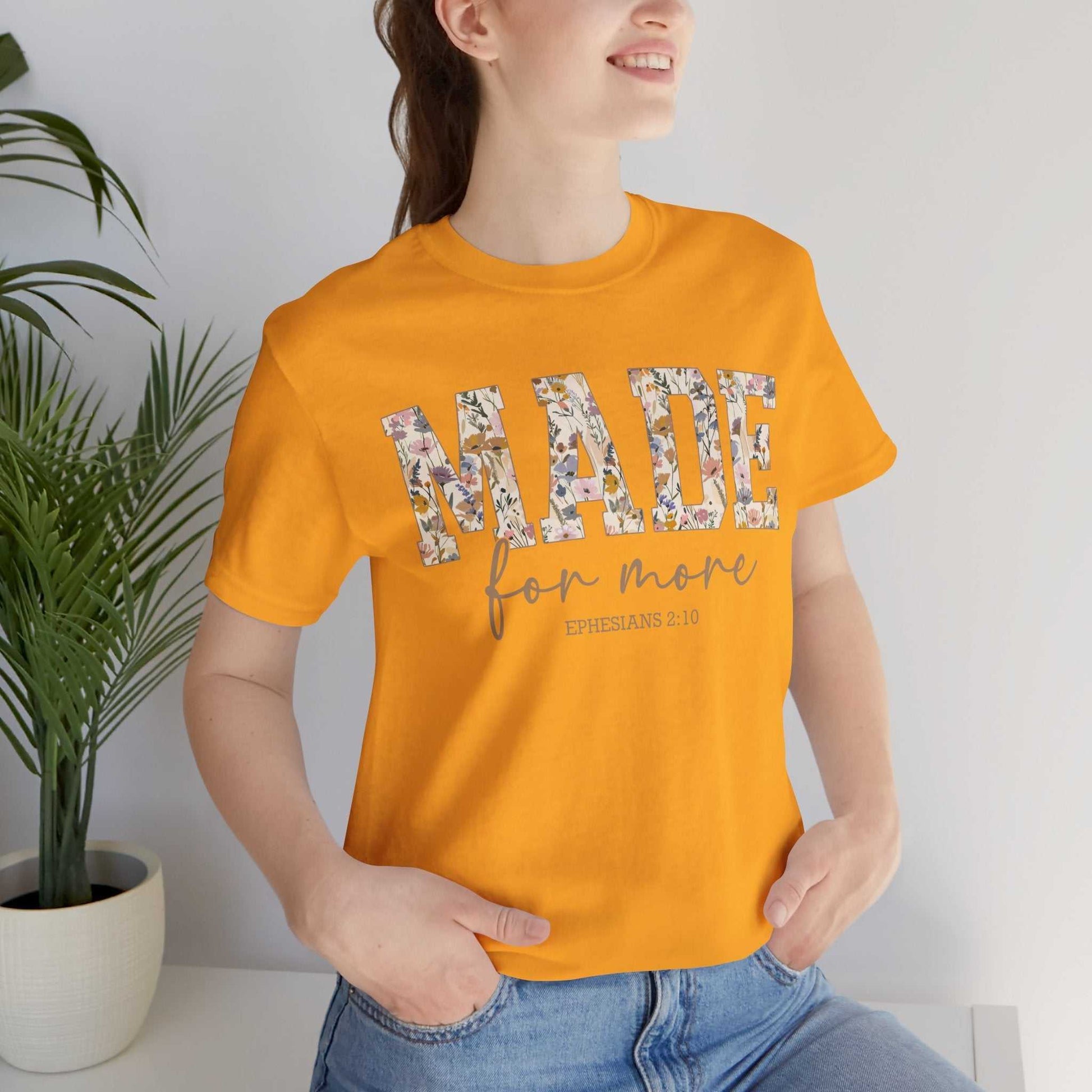 Woman wearing orange Made for More Tee with floral print text and casual pose indoors