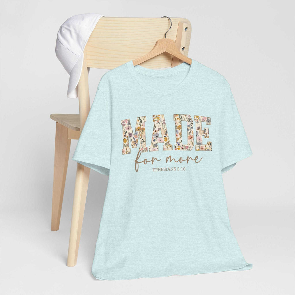 Light blue Made for More Tee with floral patterned text hanging on chair with white cap.