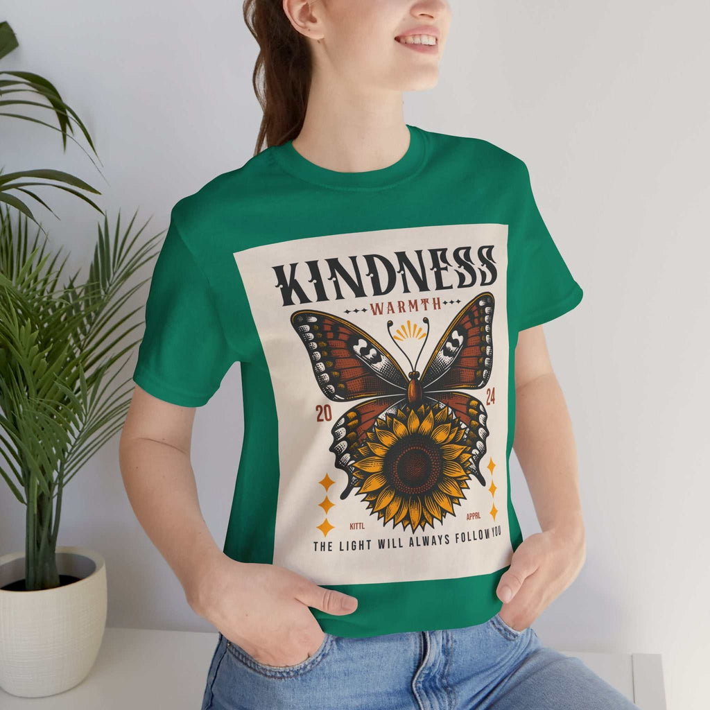 Woman wearing a green Kindness Butterfly Tee with butterfly and sunflower design and text "Kindness Warmth 2024 The light will always follow you"