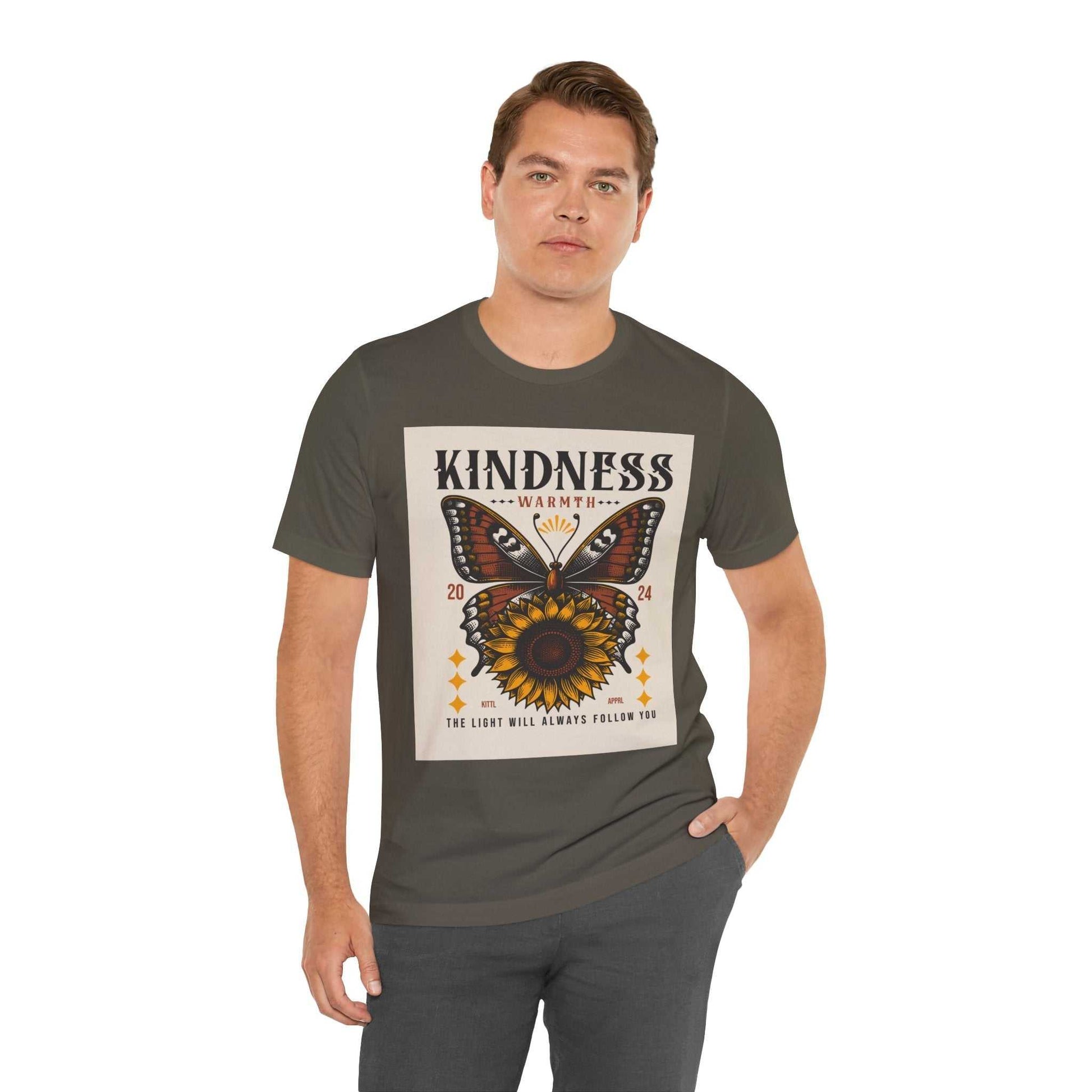 Man wearing a charcoal Kindness Butterfly Tee featuring a butterfly and sunflower graphic with the text "Kindness Warmth 2024" and "The light will always follow you"