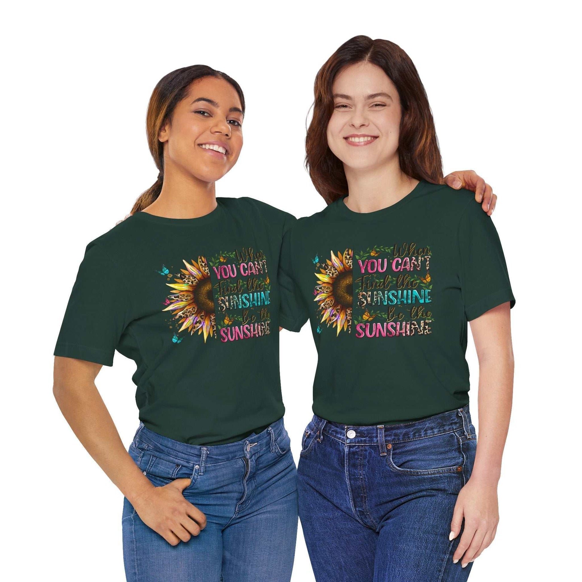 Two women wearing dark green Sunshine Quote Tee with colorful sunflower and positive quote design, smiling and posing together in casual jeans