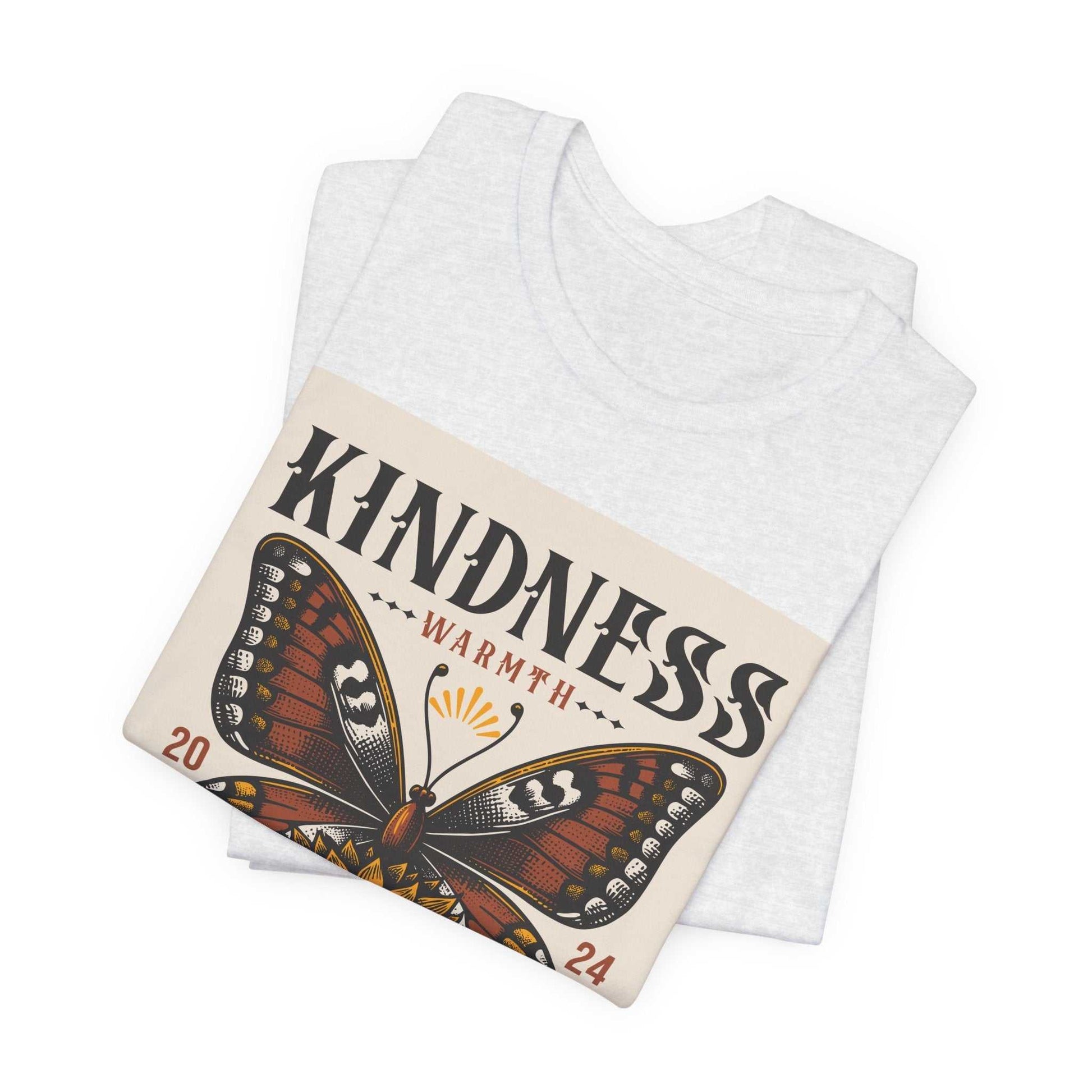Folded white t-shirt featuring a large butterfly and "Kindness Warmth 2024" graphic design on the front.