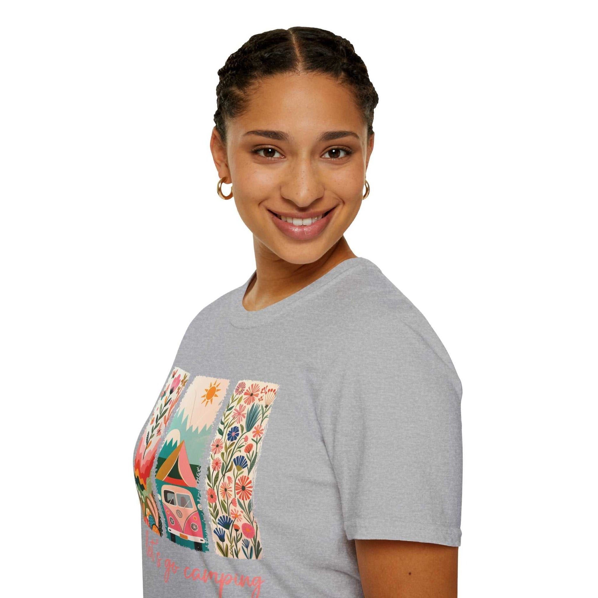 Woman wearing a gray unisex softstyle t-shirt with a colorful camping adventure design featuring a camper van and flowers.