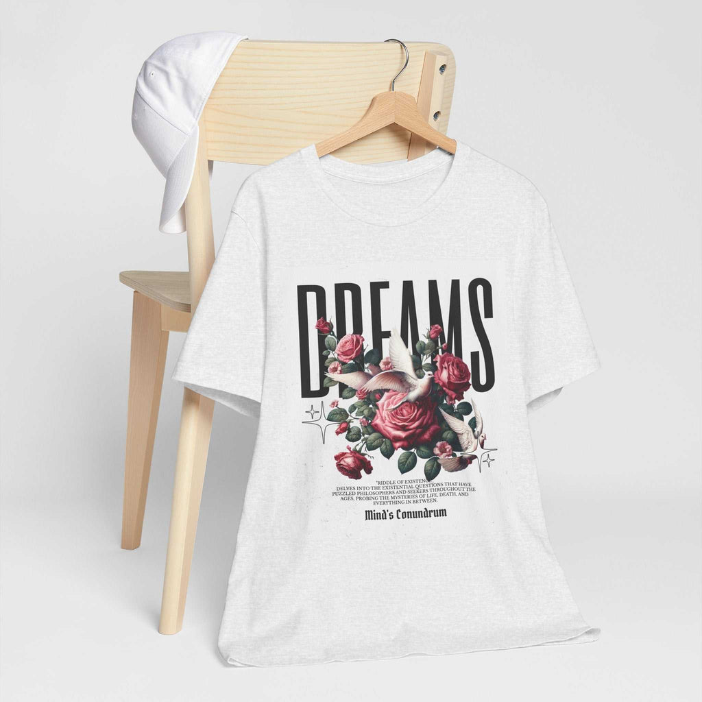 White Dreams Floral Tee with bold typography and pink rose graphic on front, displayed on wooden chair with white cap.