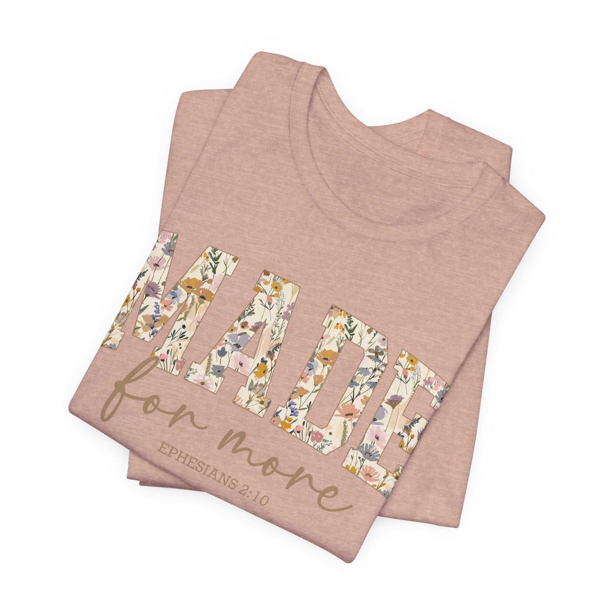Folded pink Made for More Tee with floral text design and scripture reference Ephesians 2:10