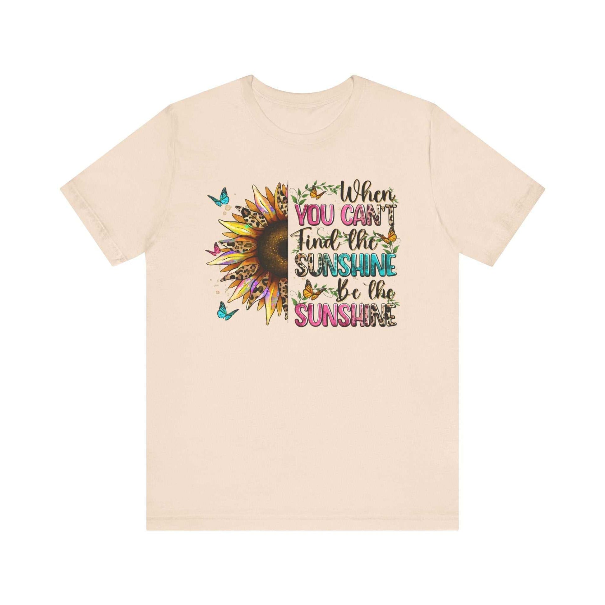Beige unisex t-shirt with colorful sunflower and butterfly design featuring the quote "When you can't find the sunshine be the sunshine"