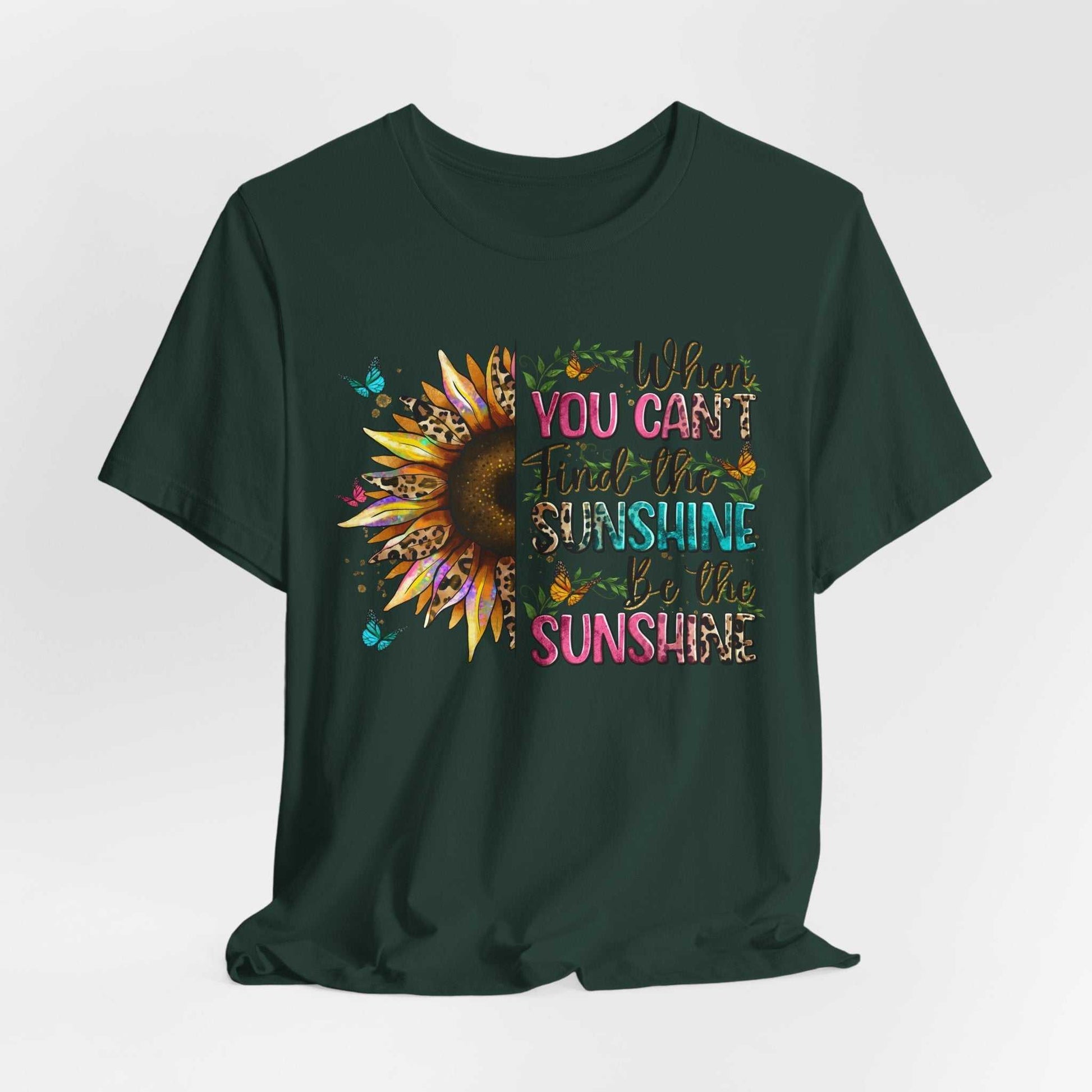Dark green unisex tee featuring a colorful sunflower and the inspirational quote "When you can't find the sunshine be the sunshine" design