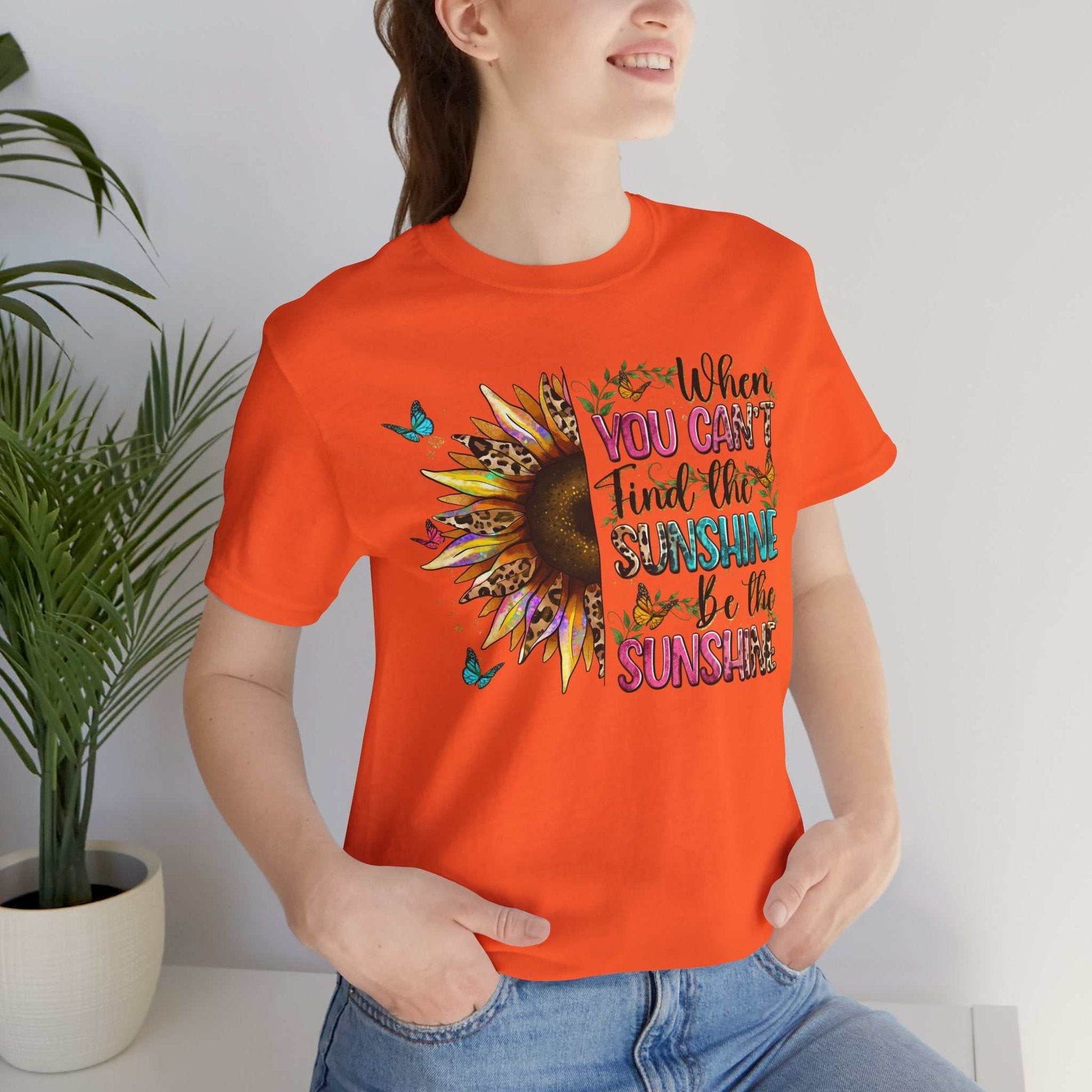 Woman wearing bright orange Sunshine Quote Tee with sunflower and motivational text design