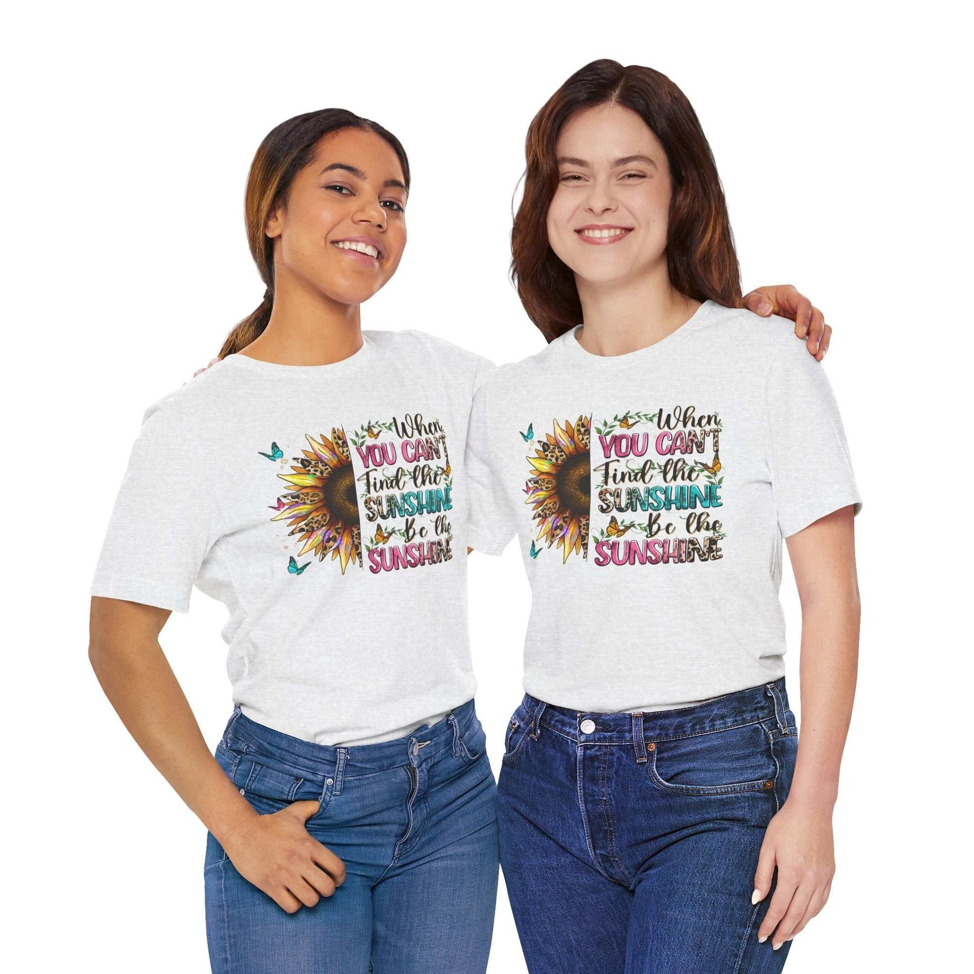 Two women wearing white Sunshine Quote Tee with colorful sunflower and positive quote design, paired with blue jeans