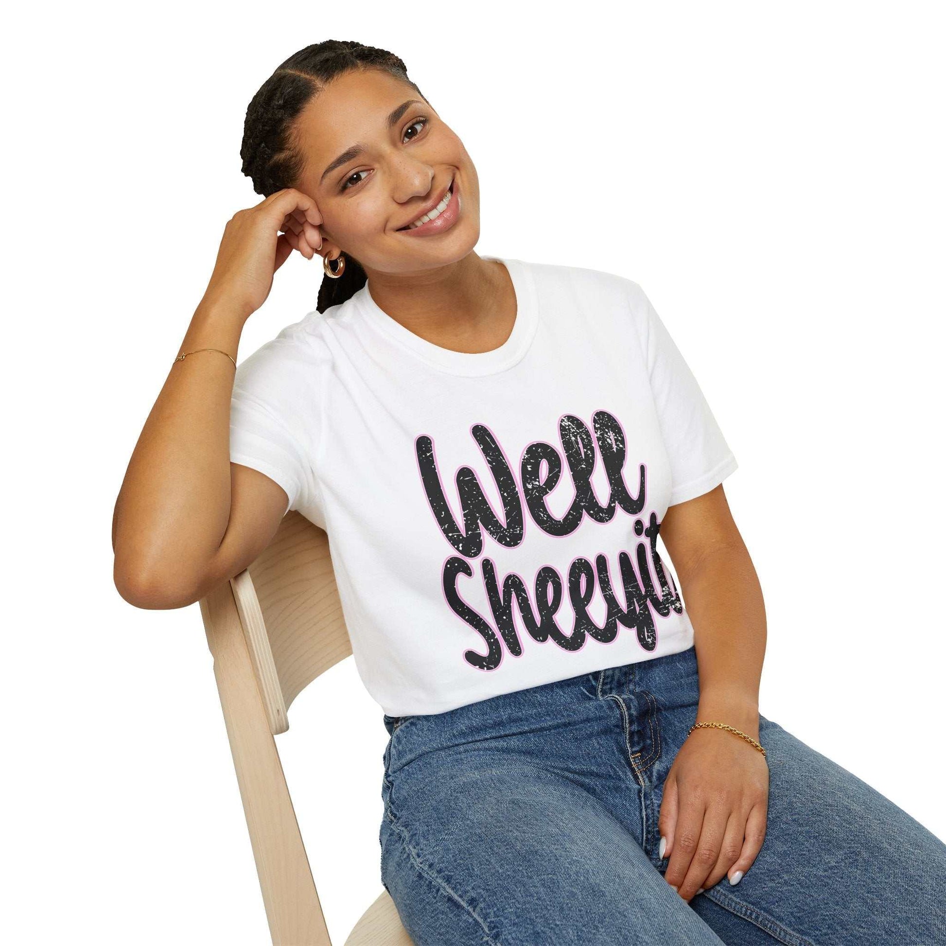 Woman wearing white casual statement tee with "Well Sheeyit" funny quote, paired with blue jeans, sitting on wooden chair