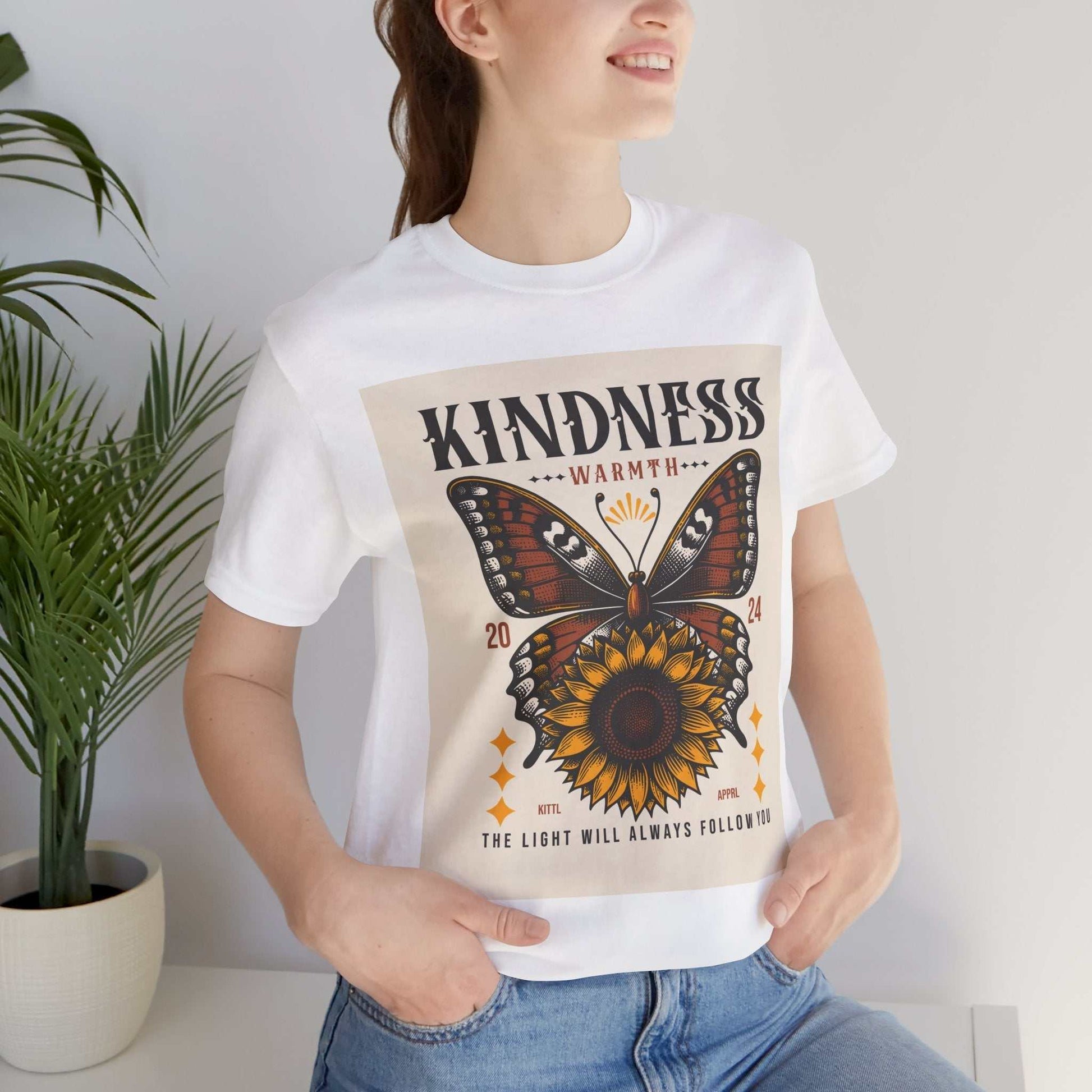 Woman wearing white Kindness Butterfly Tee with butterfly and sunflower graphic and text "The light will always follow in"