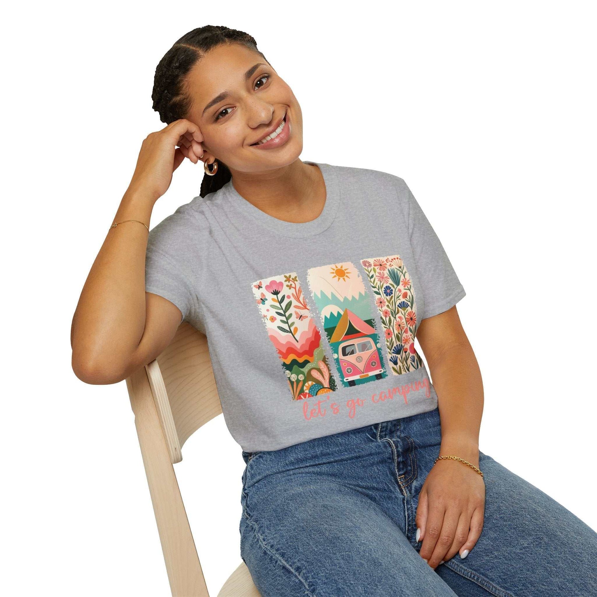 Unisex softstyle gray t-shirt with colorful Camping Adventure graphic design featuring nature and a camper van, worn by smiling woman sitting on chair.