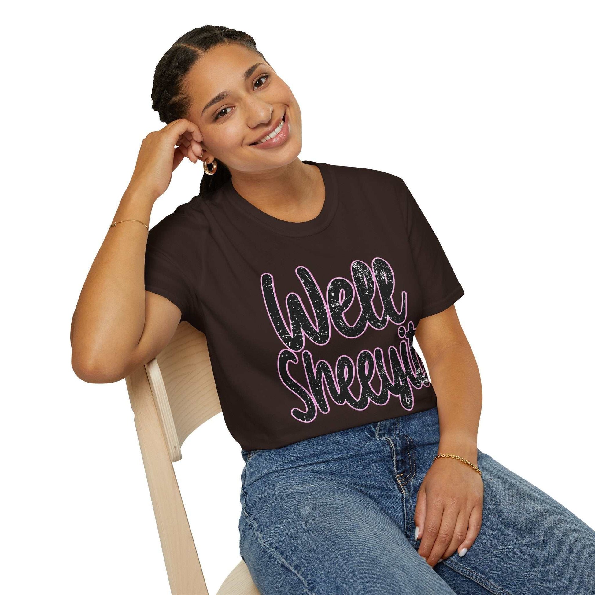 Woman wearing black casual statement tee with "Well Sheeyit" humorous quote sitting on chair smiling