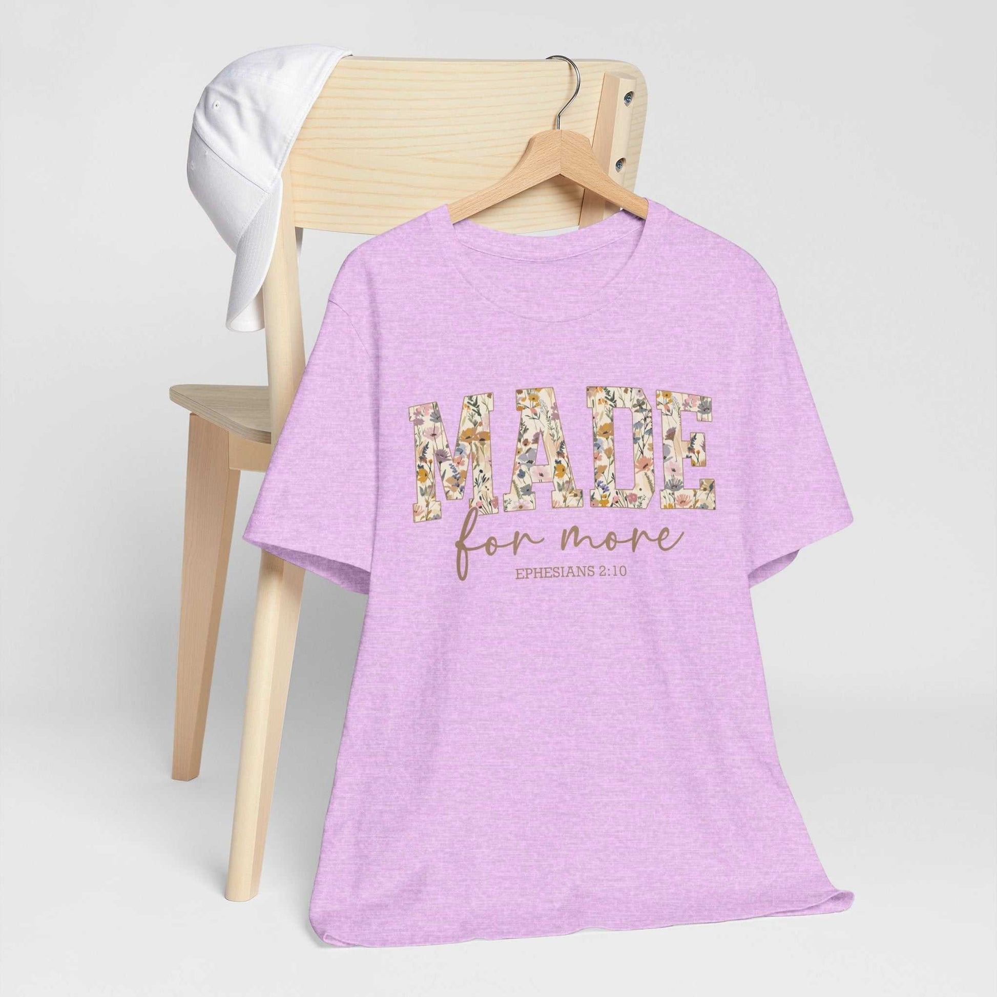 Purple Made for More Tee with floral design text hanging on wooden chair with white cap