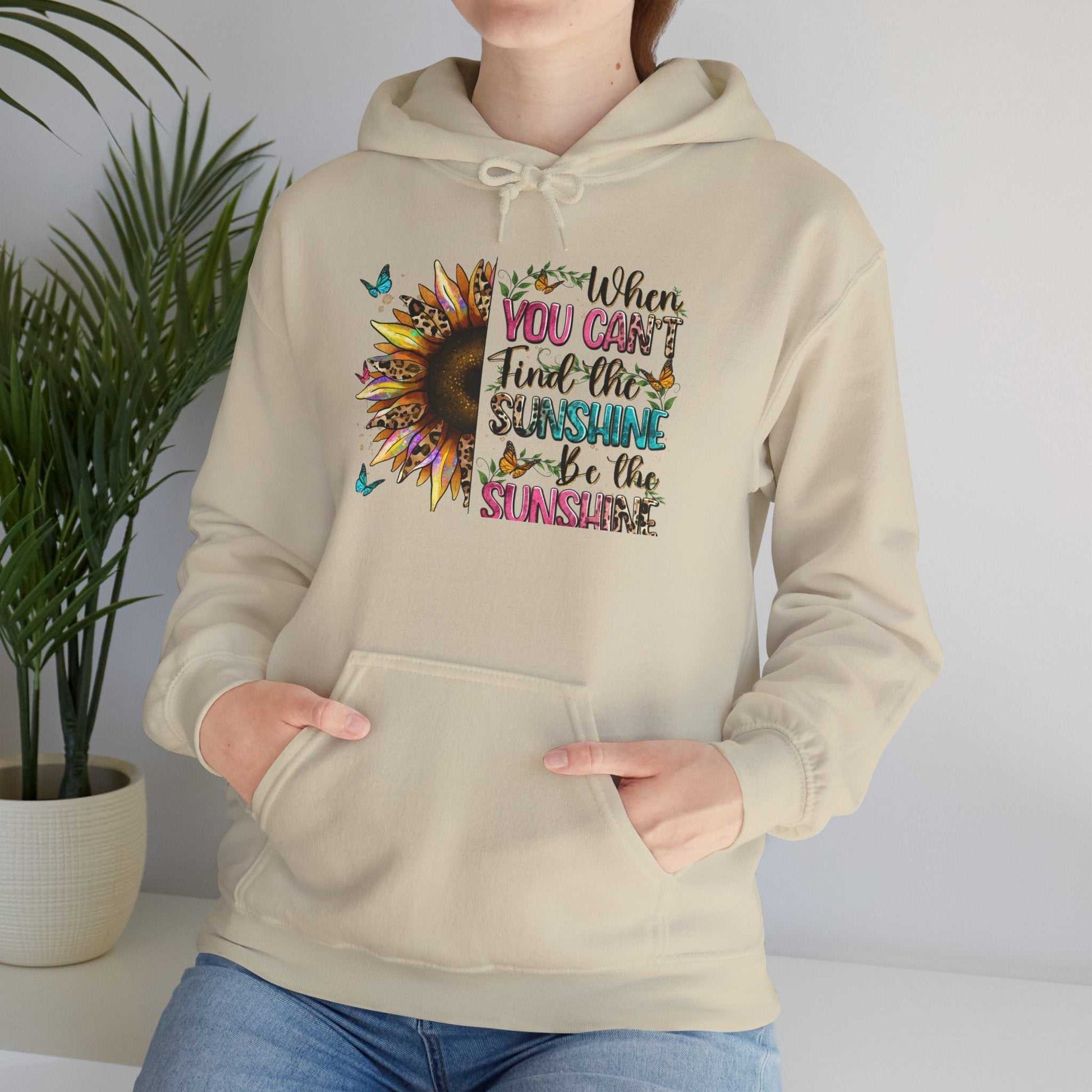 Person wearing beige sunflower quote hoodie with inspirational text and sunflower graphic on front, kangaroo pocket, and adjustable drawstring hood