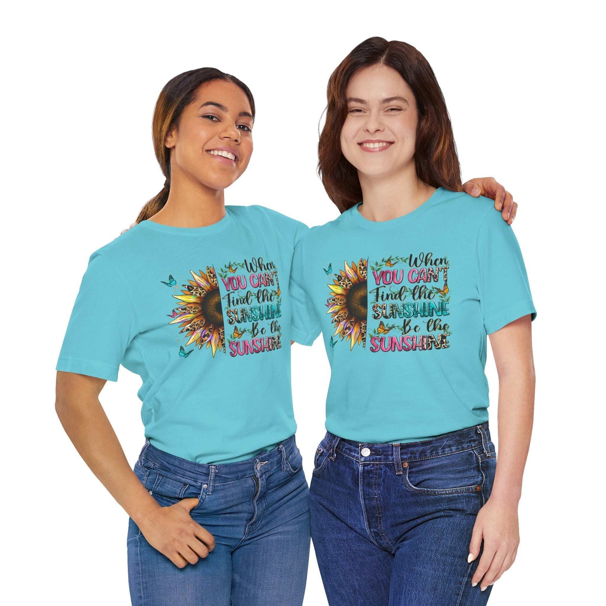 Two women wearing light blue Sunshine Quote Tee with colorful sunflower and inspirational text design, paired with jeans