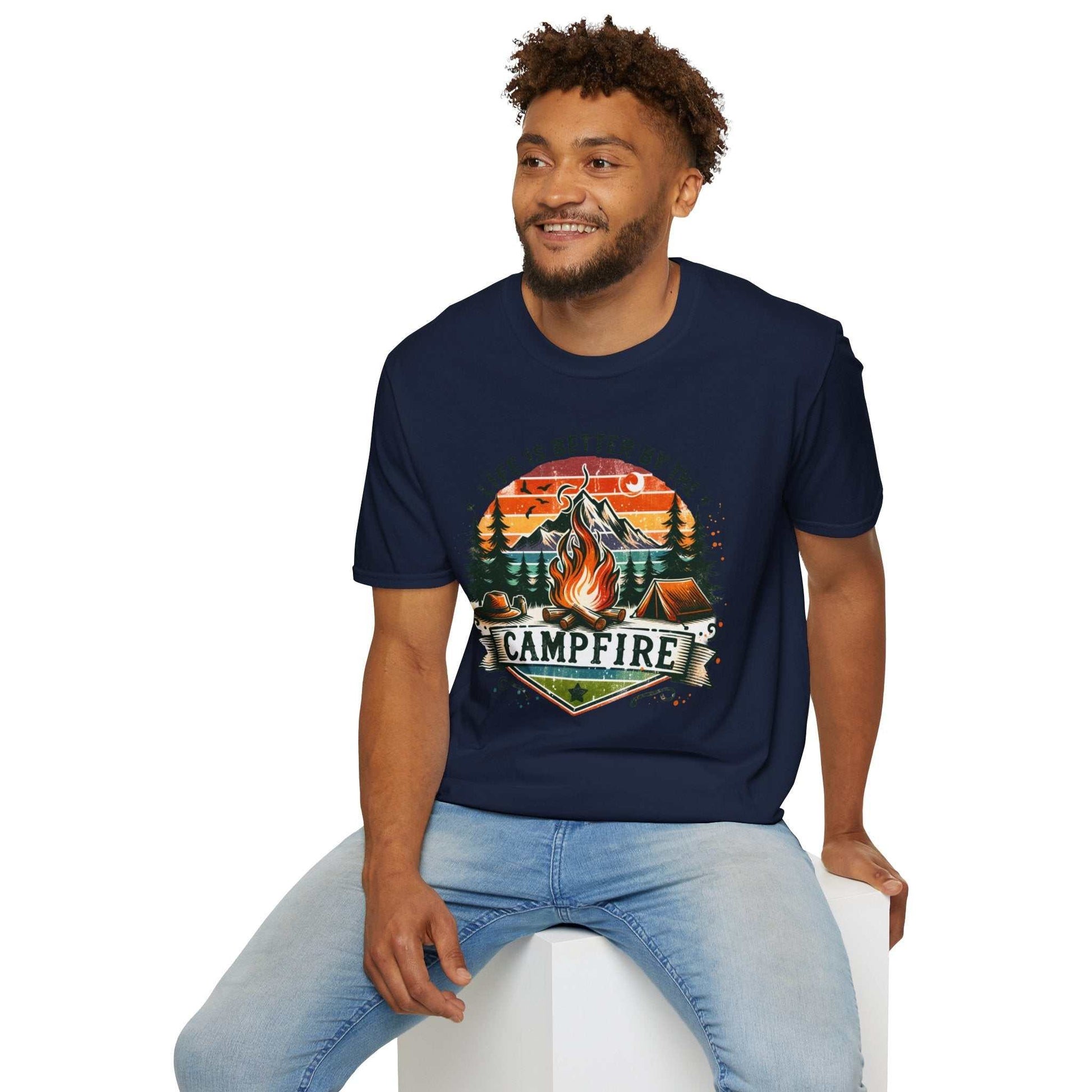 Man wearing navy Camping Adventure Unisex T-Shirt with colorful campfire graphic sitting on white block