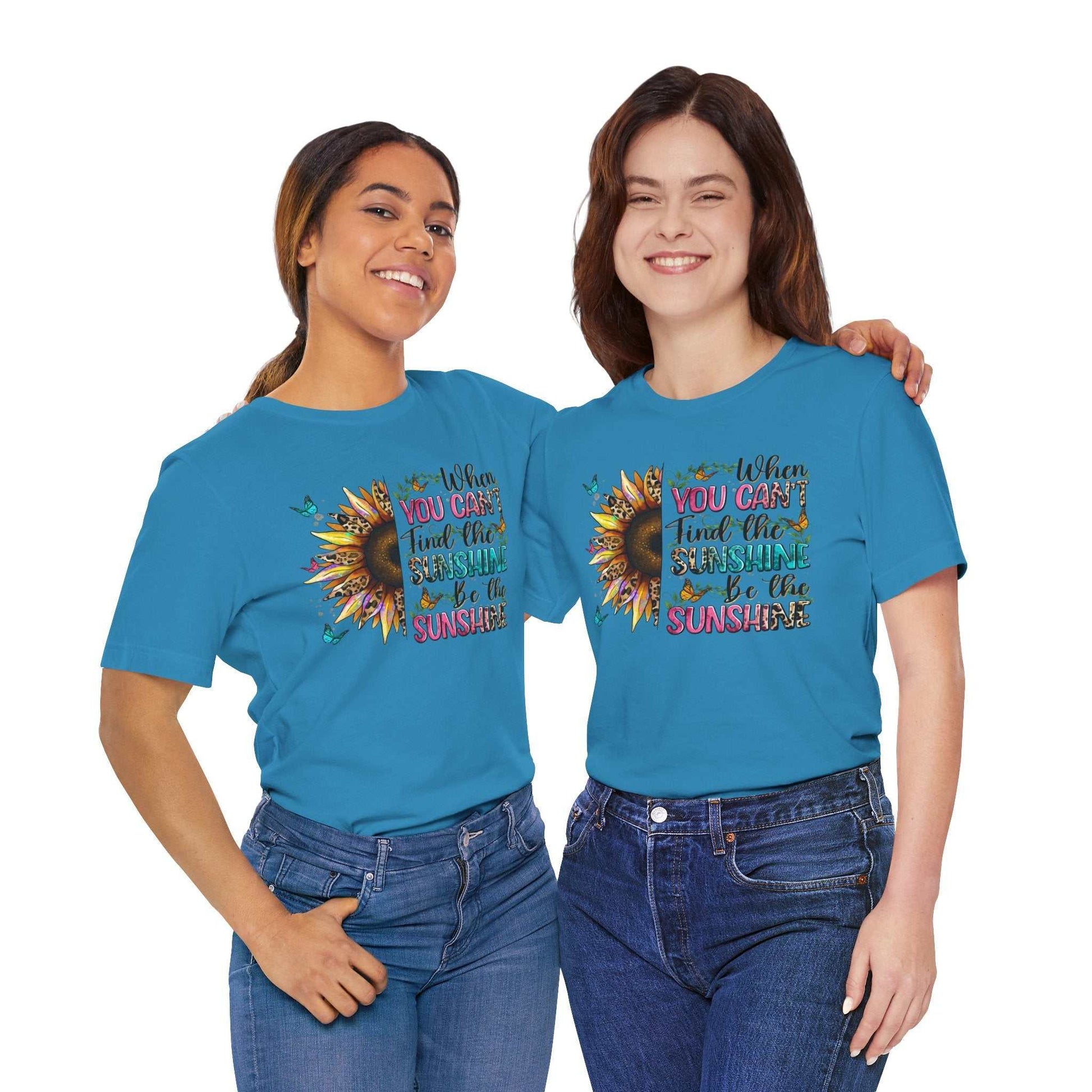 Two women wearing blue Sunshine Quote Tee with colorful sunflower graphic and inspirational text "When you can't find the sunshine, be the sunshine"